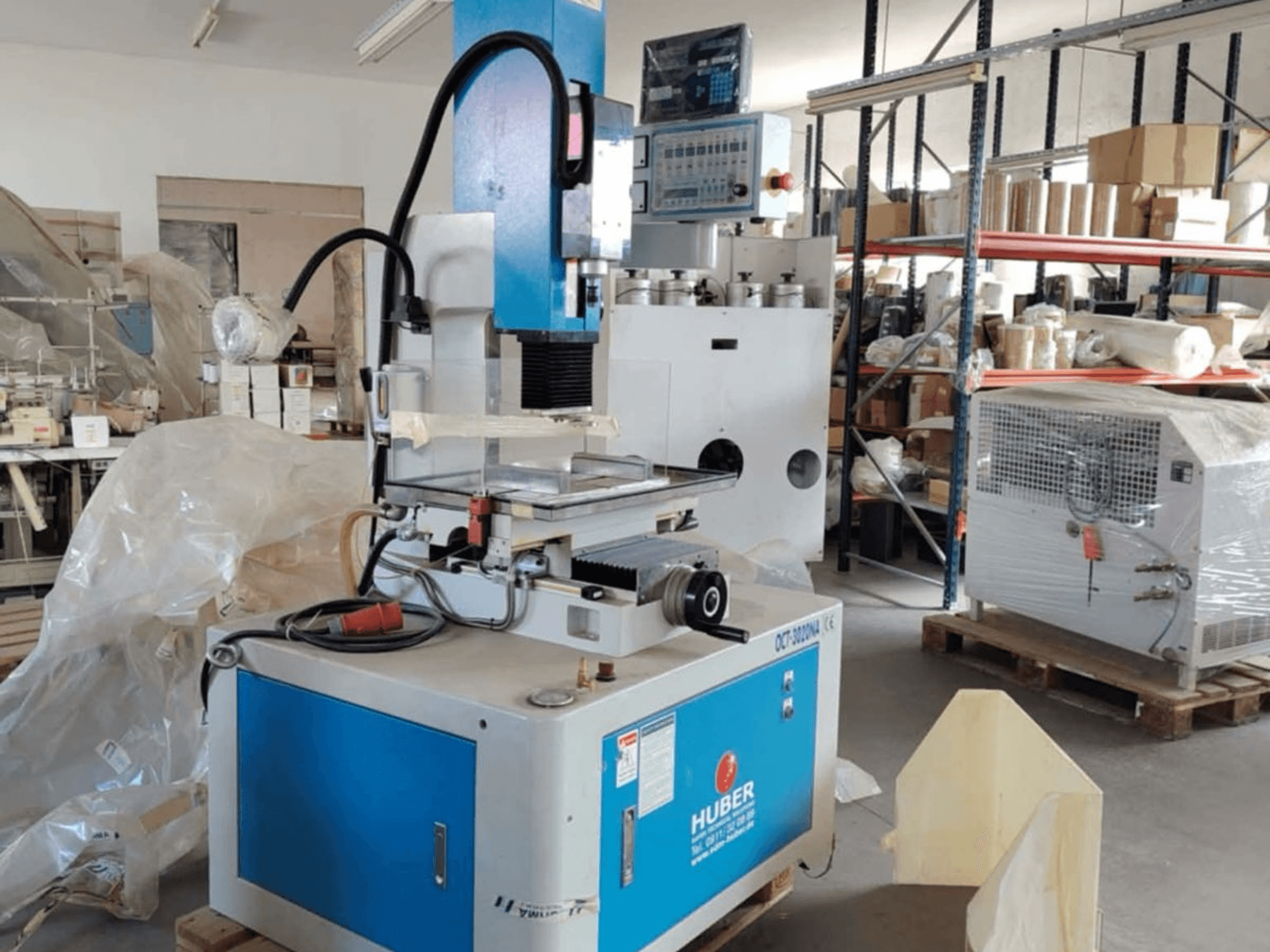 Elektrodrążarka wgłębna HUBER OCT-3020 NA w warsztacie, widok z przodu przedstawiający niebiesko-szarą obudowę, cyfrowe elementy sterujące i obszar roboczy.