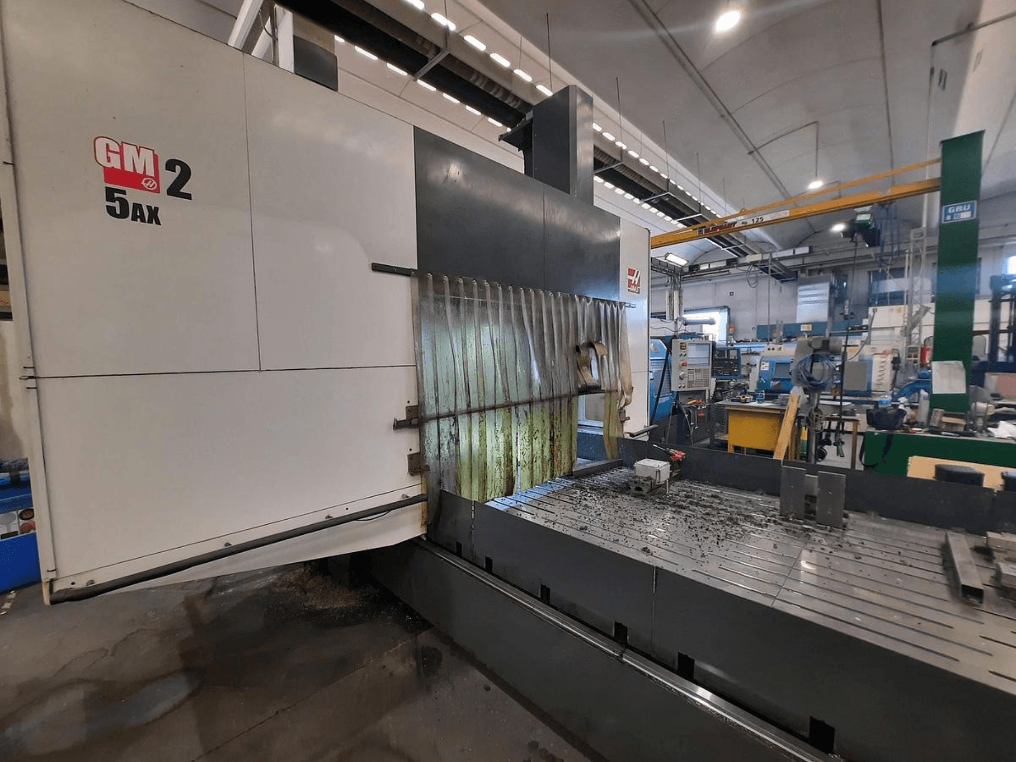Maszyna CNC GM 2 5AX w warsztacie, widok z boku, pokazujący obszar roboczy i wióry metalowe na powierzchni łoża.