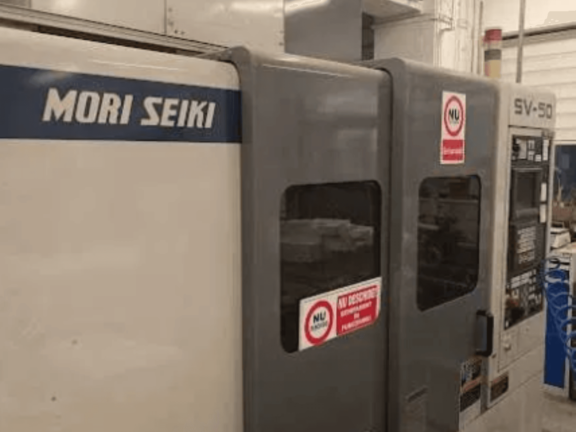 Maszyna CNC MORI SEIKI SV-50, widok z boku; posiada panel sterowania i naklejki ostrzegawcze.