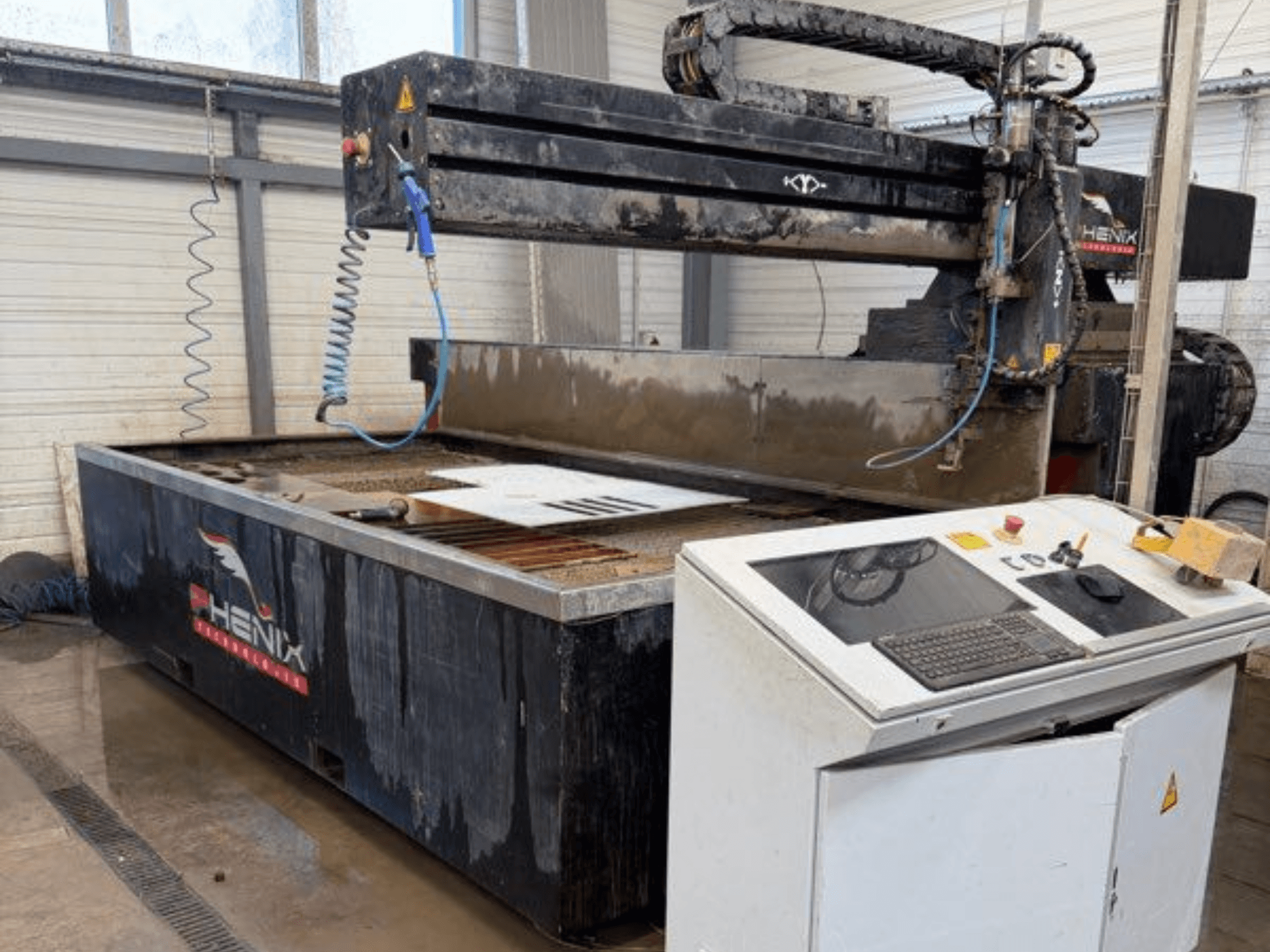 Maszyna do cięcia strumieniem wody PHENIX MD JET 1530, widok z przodu przedstawiający panel sterowania i obszar cięcia z widocznym zbiornikiem wody.