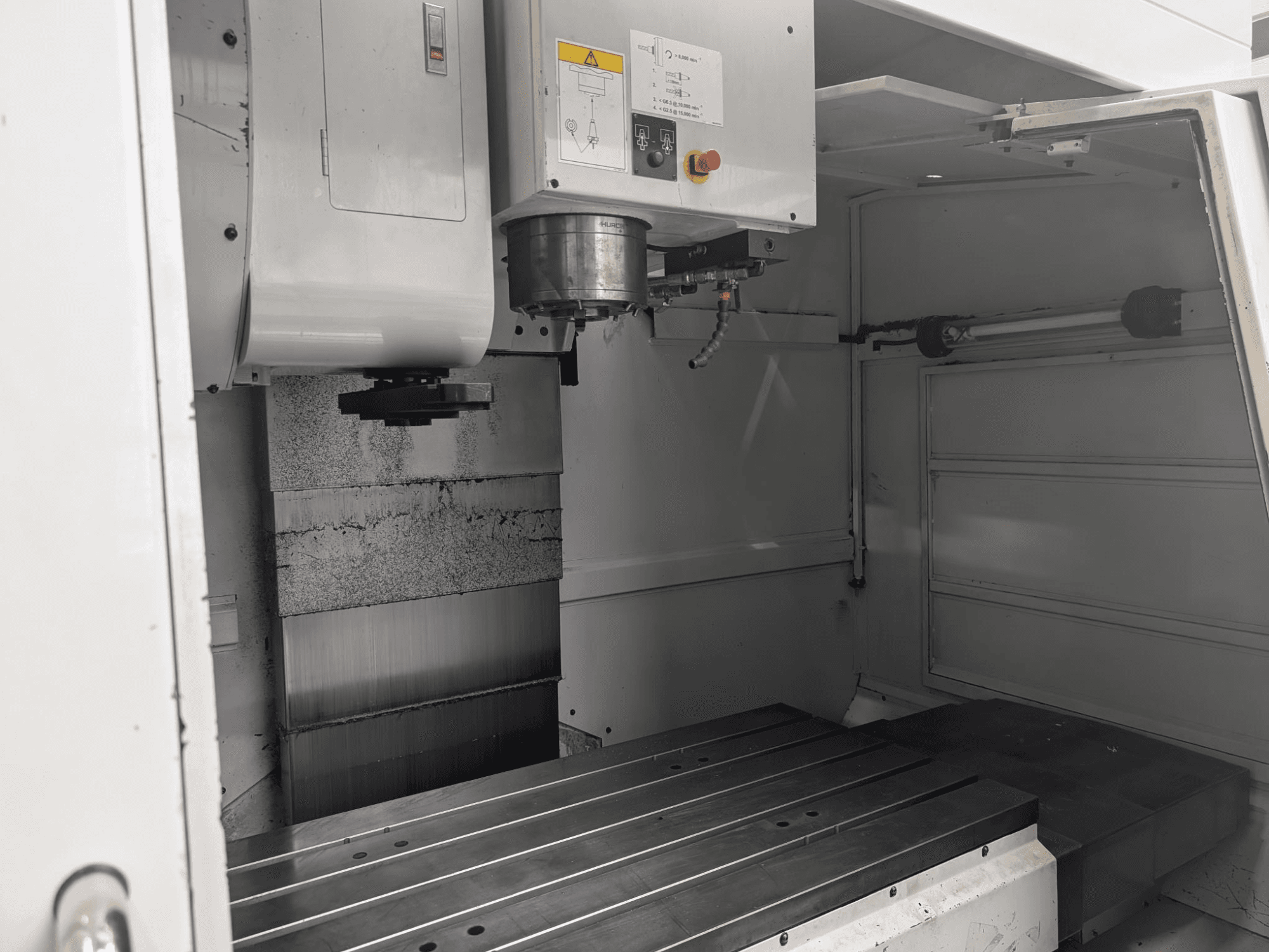 Widok wnętrza frezarki CNC z dużym metalowym stołem roboczym i silnikiem wrzeciona, pokazujący szczegółowe komponenty i panel sterowania.