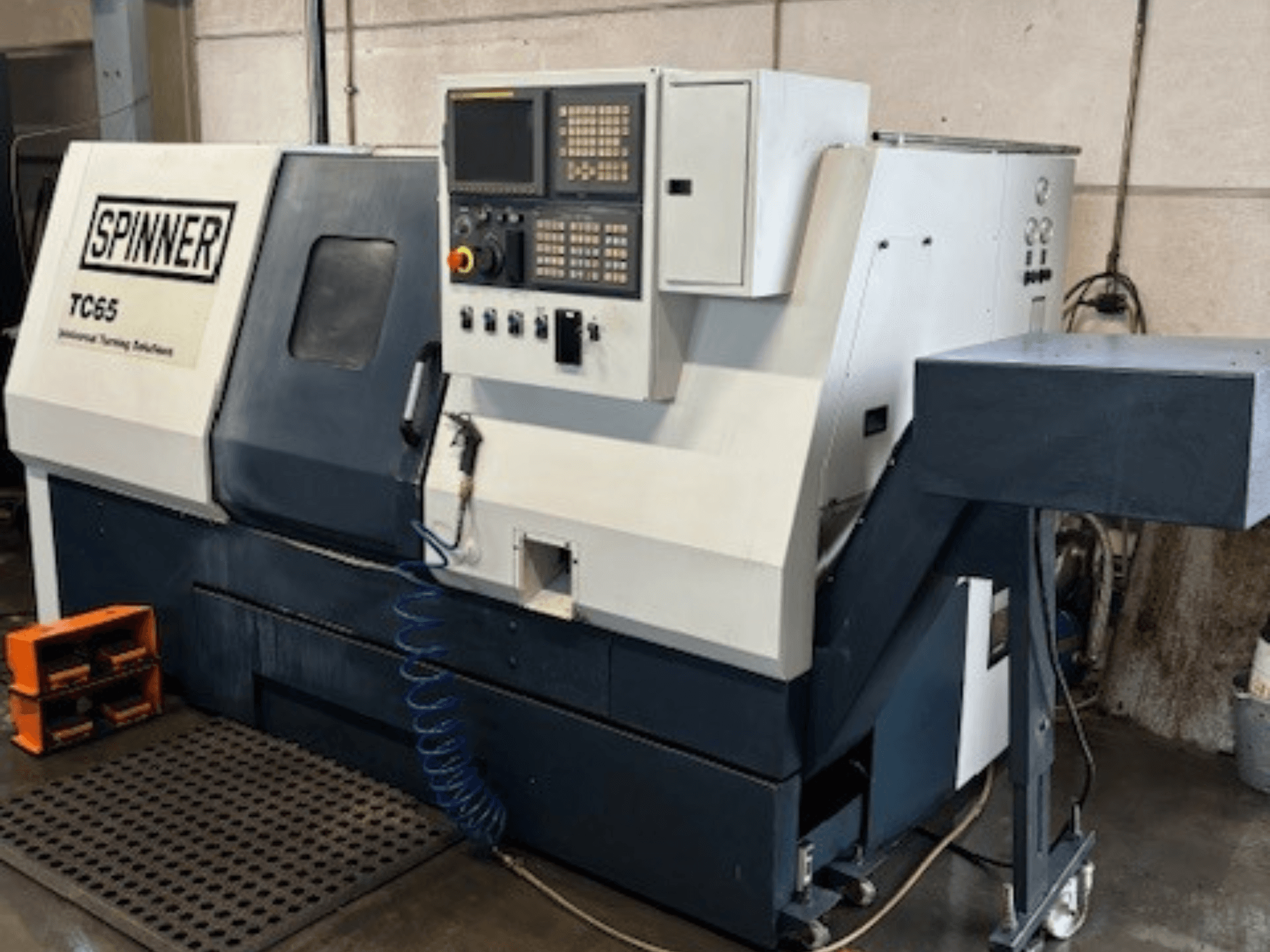 Przemysłowa tokarka Spinner TC65, widok z przodu, z panelem sterowania, przewodem sprężonego powietrza i schowkiem na narzędzia.
