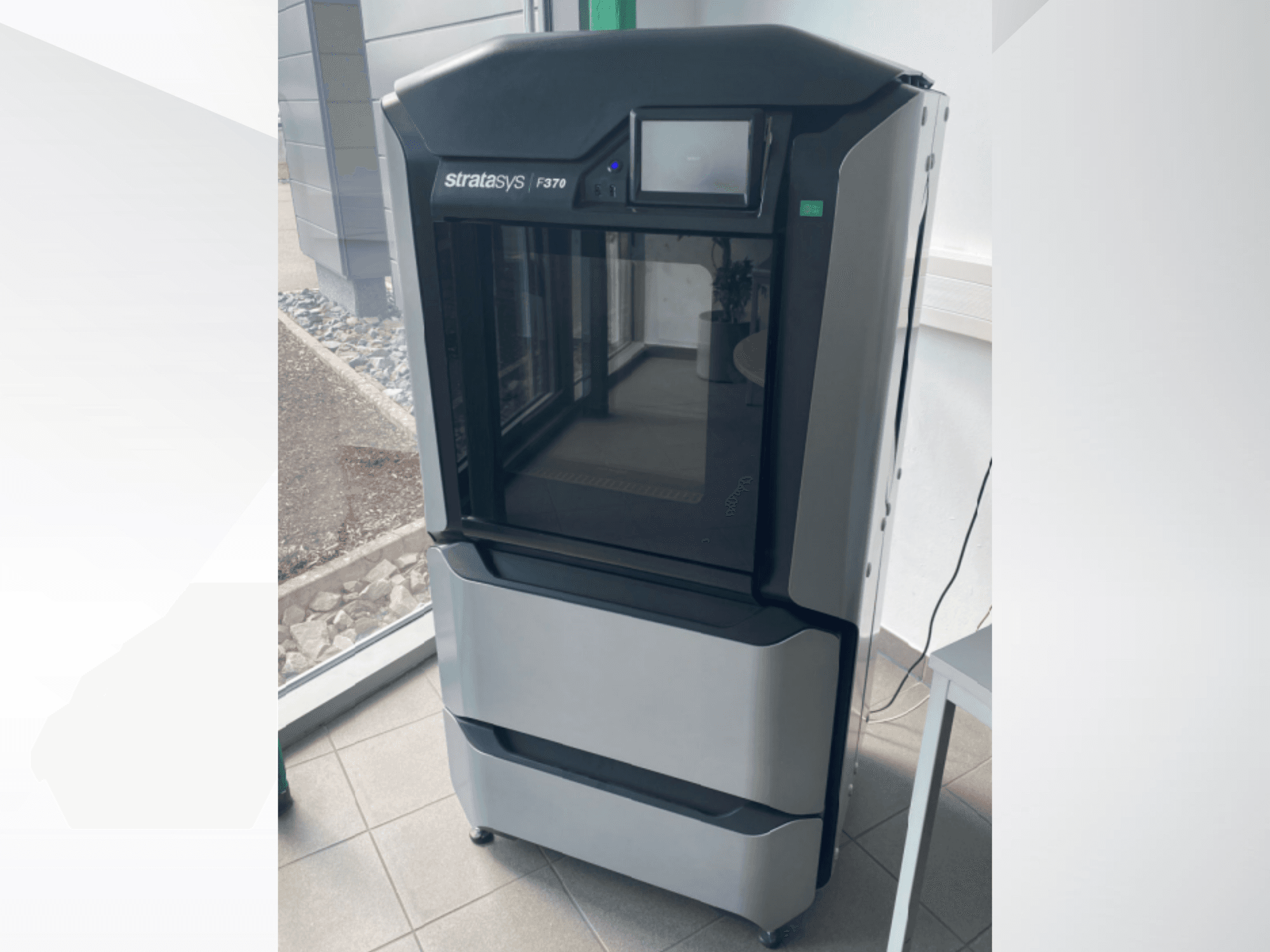 Drukarka 3D do tworzyw sztucznych Stratasys F370, widok z przodu, elegancka czarno-szara konstrukcja z ekranem dotykowym.