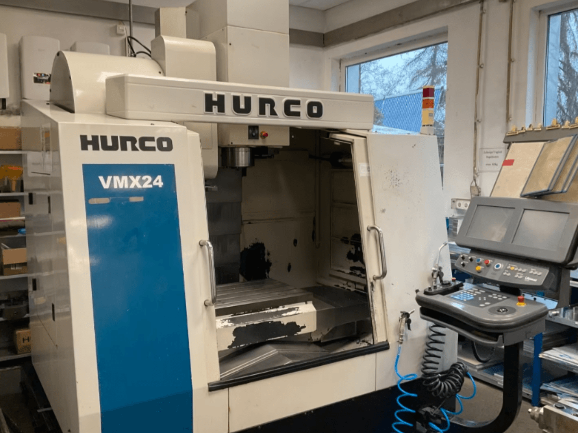 Pionowe centrum obróbcze Hurco VMX24 widziane z przodu, z widocznym panelem sterowania, głowicą wrzeciona i obszarem roboczym; widać ślady zużycia.