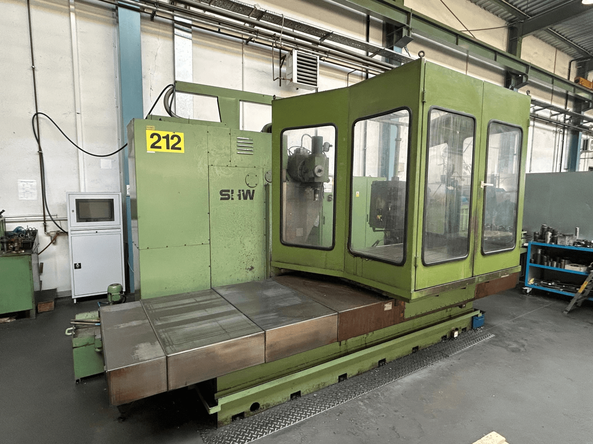 Pionowe centrum obróbcze SHW UF-5 w kolorze zielonym, widok z przodu przedstawiający panel sterowania, szklaną obudowę i metalowy stół roboczy.