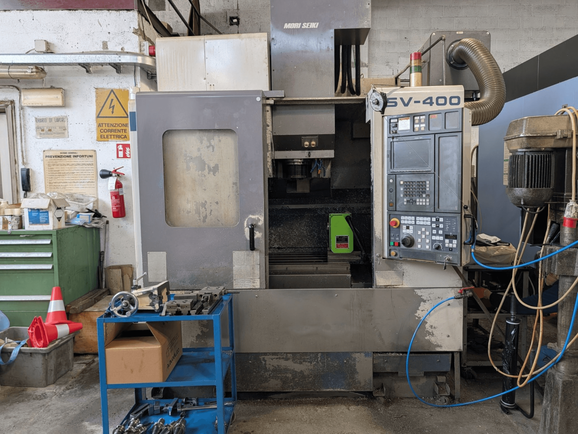 Pionowe centrum obróbcze MORI SEIKI SV-400 w warsztacie, widok z boku, panel sterowania i obrabiarki w pobliżu.