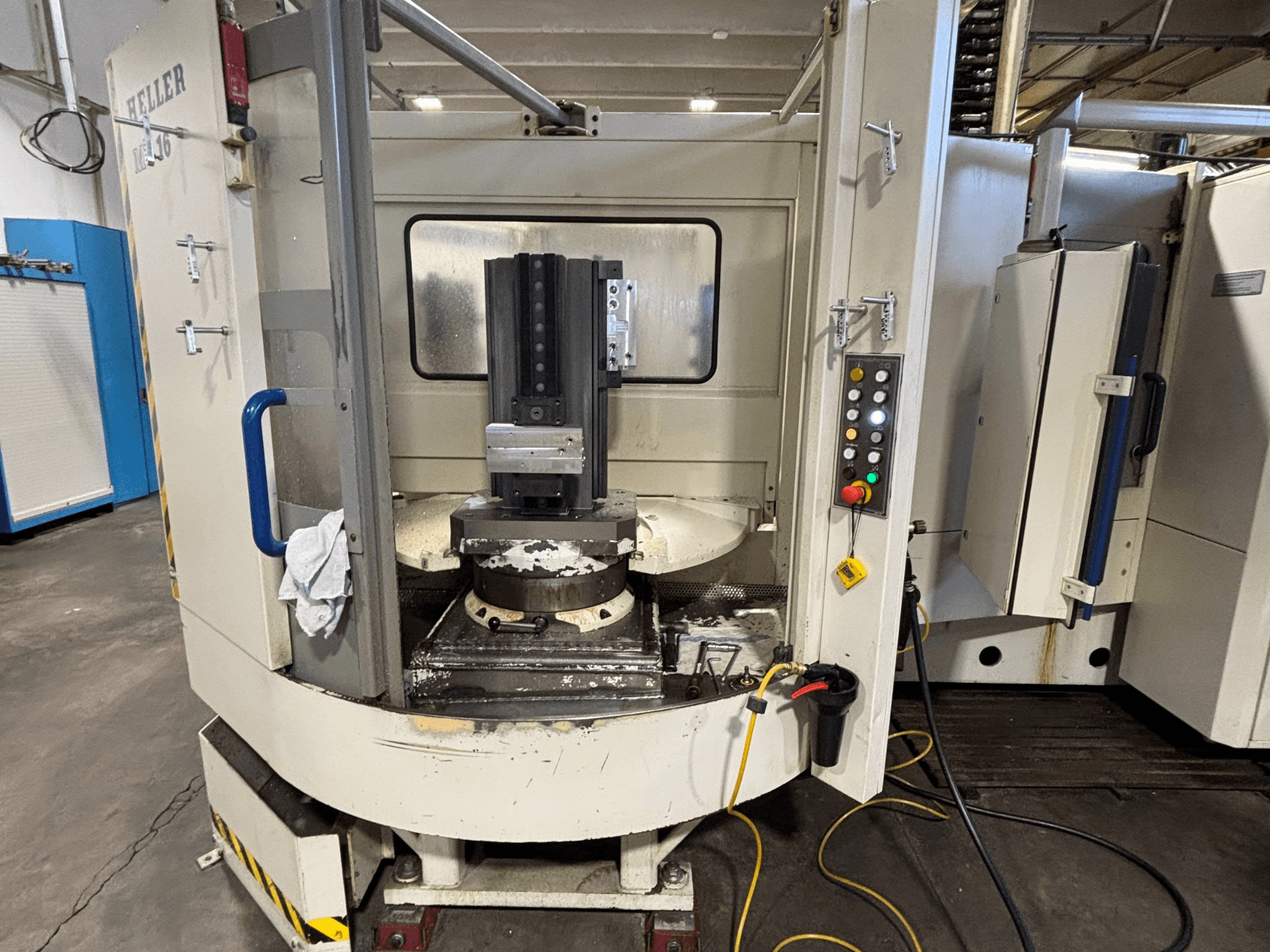 Centrum obróbcze Heller, model pionowy, widok z przodu przedstawiający wrzeciono, panel sterowania i stół roboczy z zamontowanym wyposażeniem.