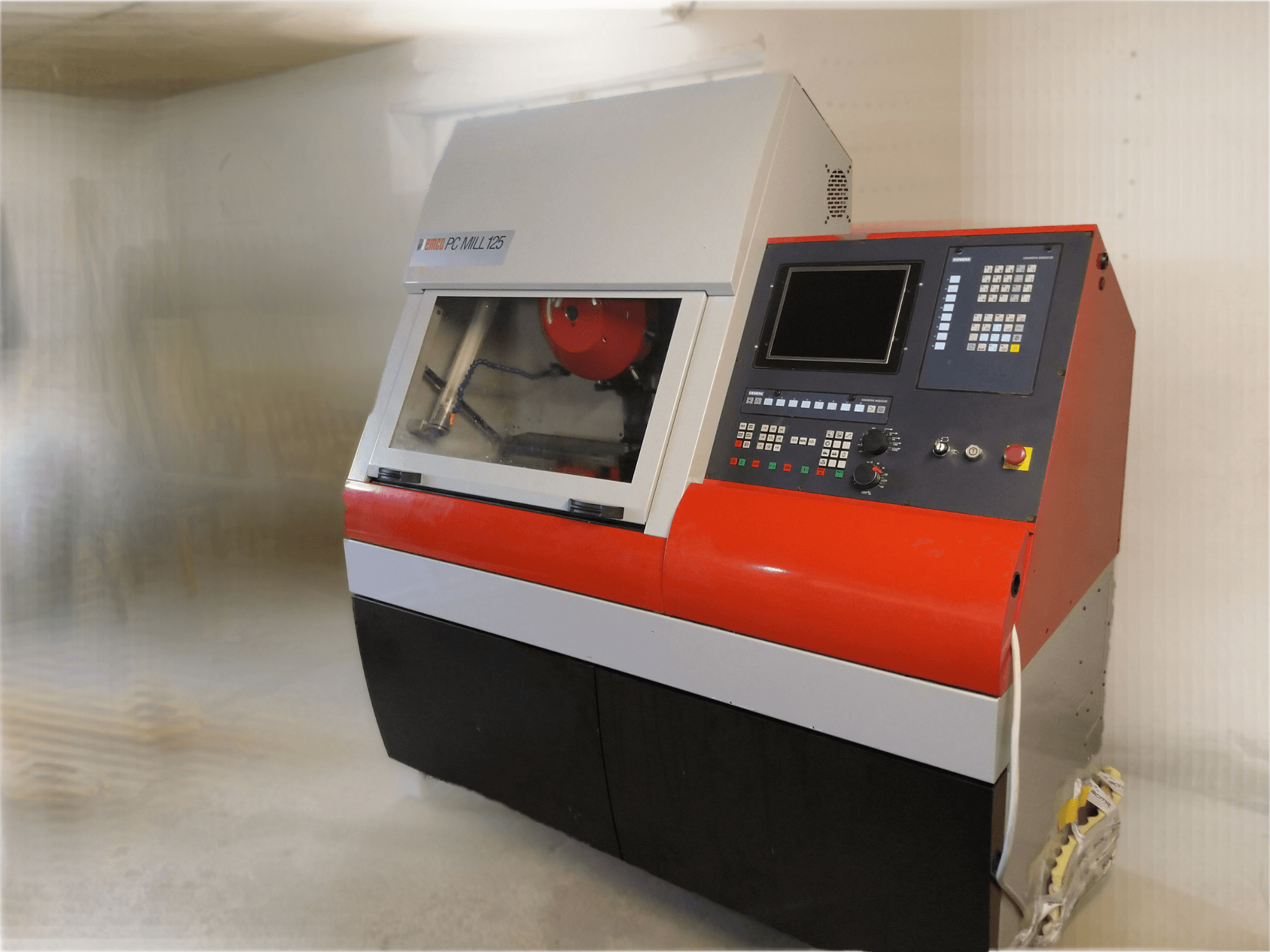 Pionowe centrum obróbcze EMCO PC MILL 125, widok z przodu z panelem sterowania i widocznym obszarem obróbki.