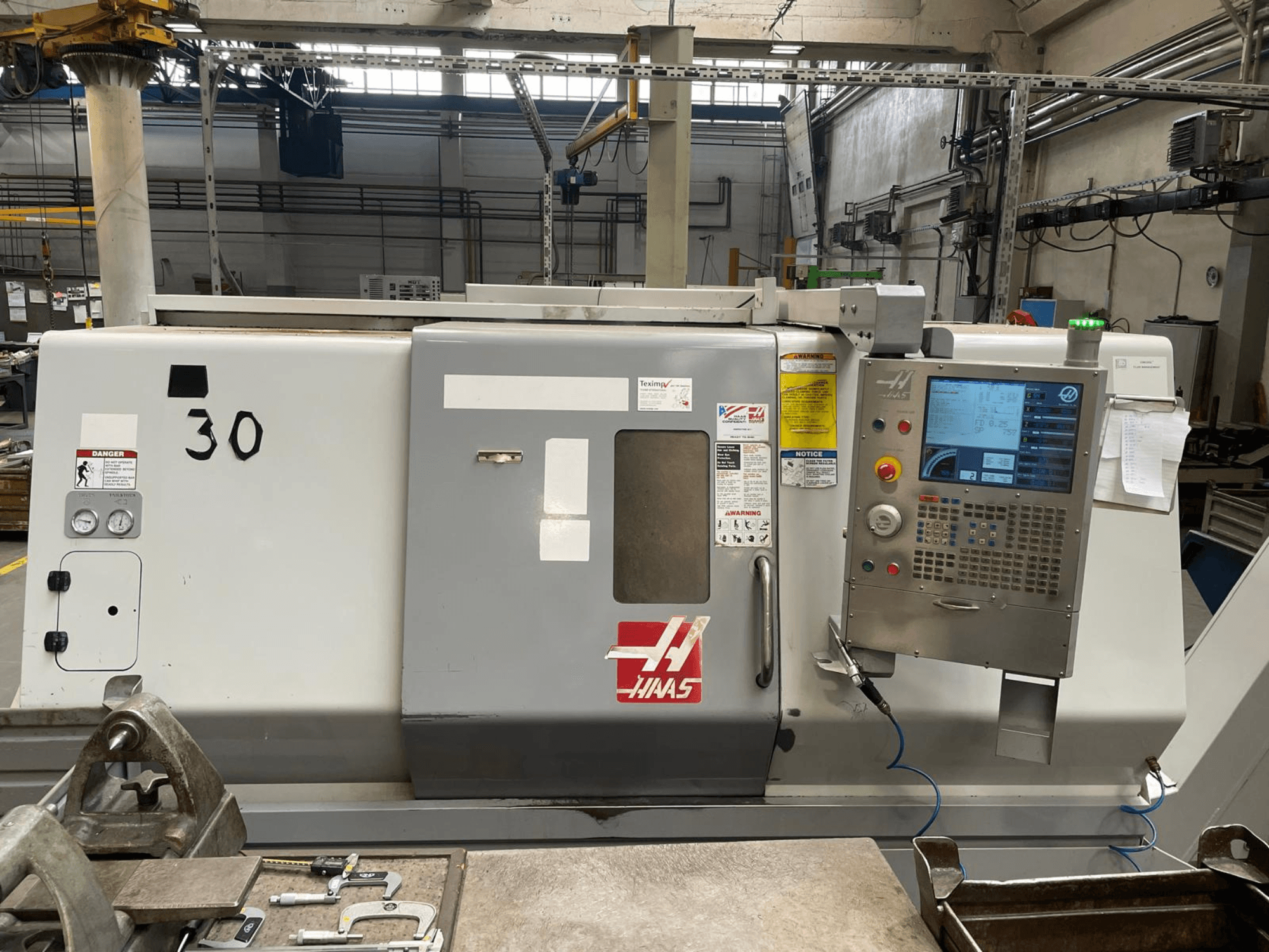 Widok z przodu tokarki poziomej Haas SL-30THE, na którym widoczny jest cyfrowy panel sterowania, etykiety ostrzegawcze oraz numer modelu 30.