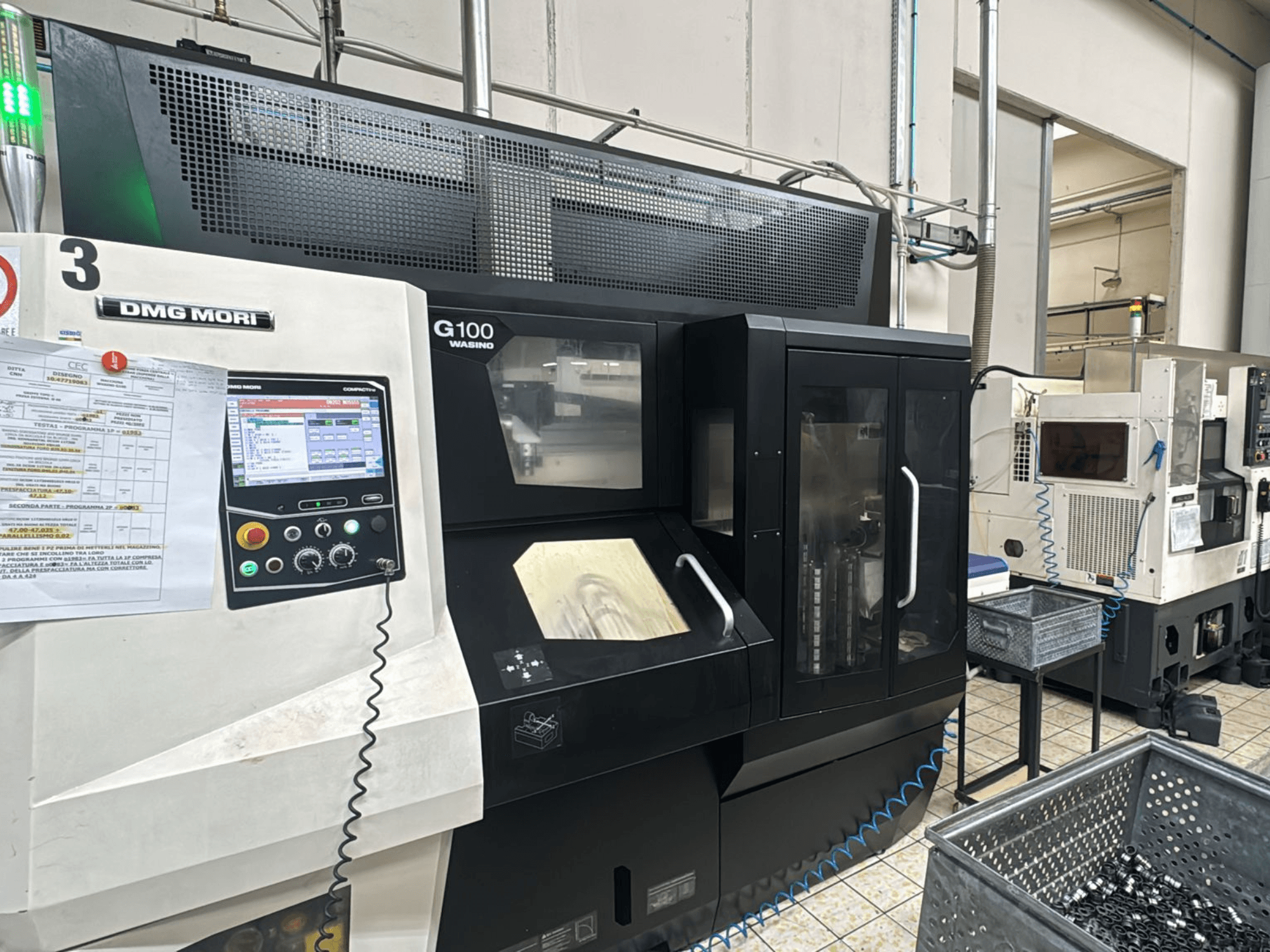 Maszyna DMG MORI G100 w fabryce, widok z przodu, z cyfrowym panelem sterowania i pobliskimi pojemnikami na narzędzia.