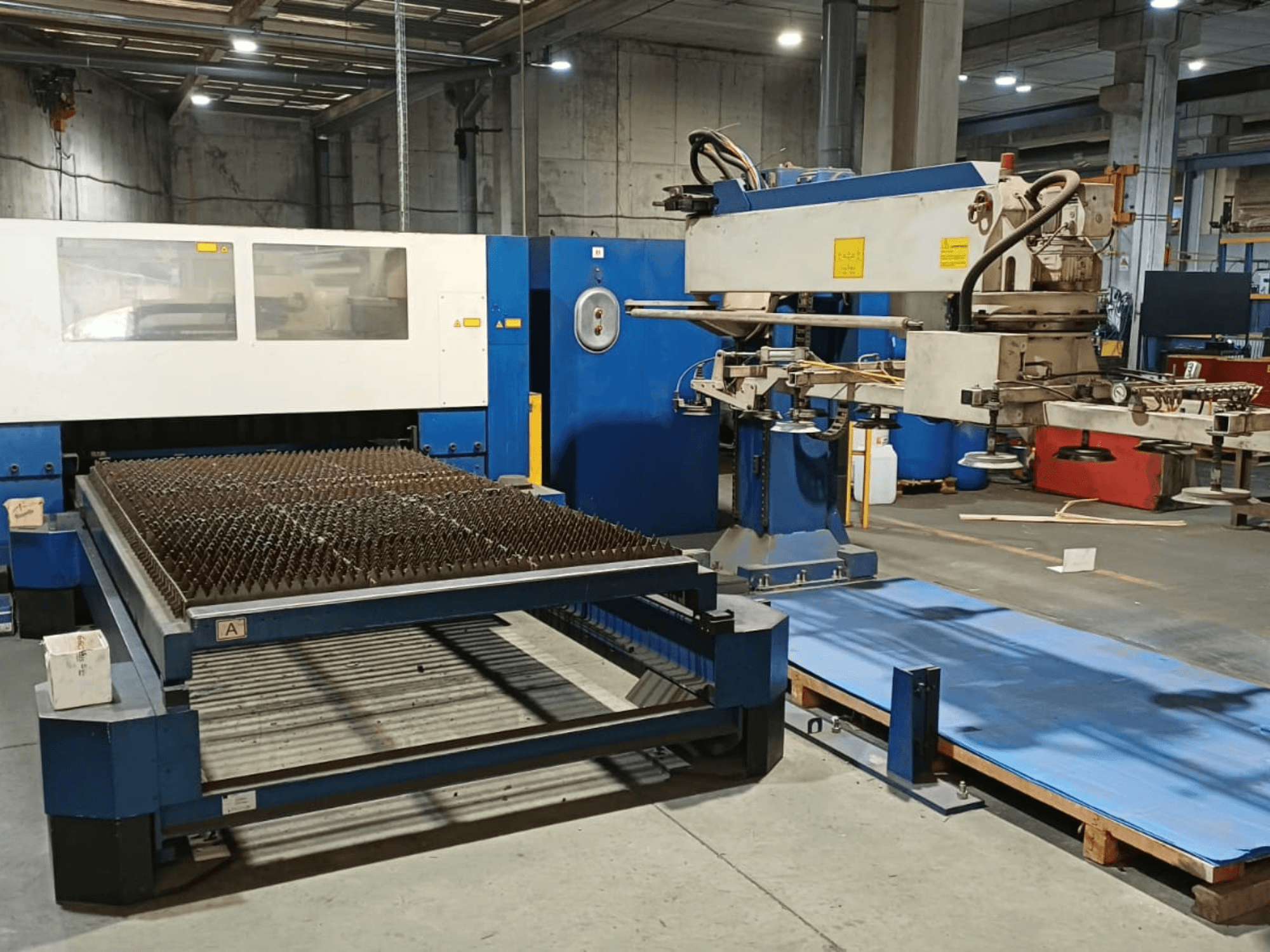 Maszyna do cięcia laserowego CO₂ TRUMPF TRUMATIC L 3030, widok z boku, przedstawiająca stół do cięcia z powierzchnią kolczastą oraz ramię robota.