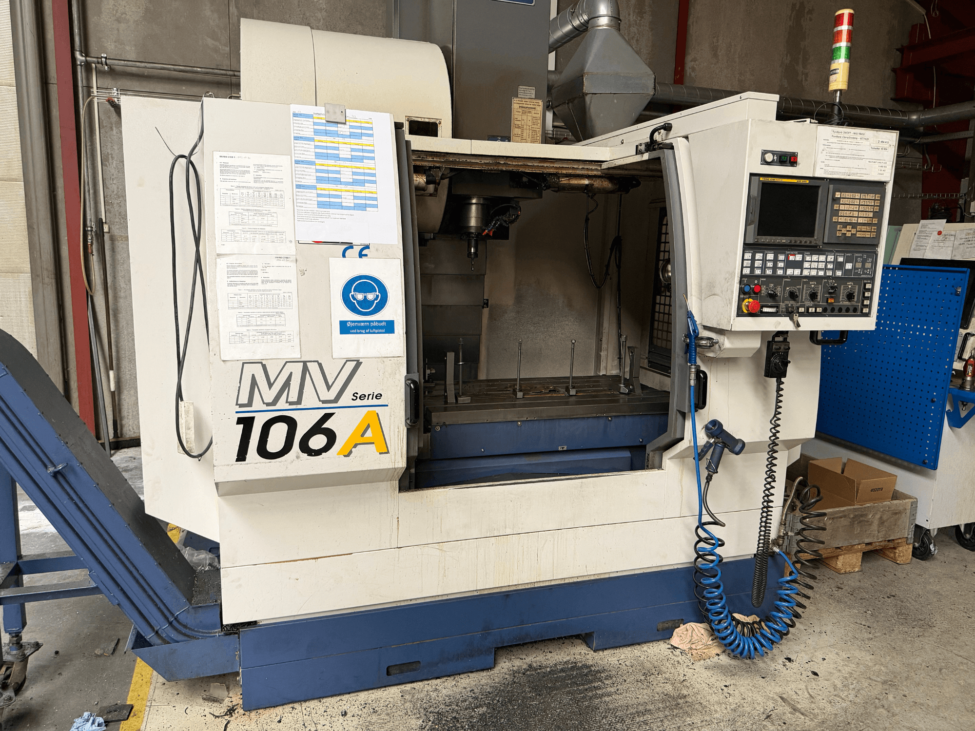 Pionowe centrum obróbcze YCM MV106A, widok z przodu przedstawiający panel sterowania i obszar roboczy, wraz z dołączoną dokumentacją techniczną.