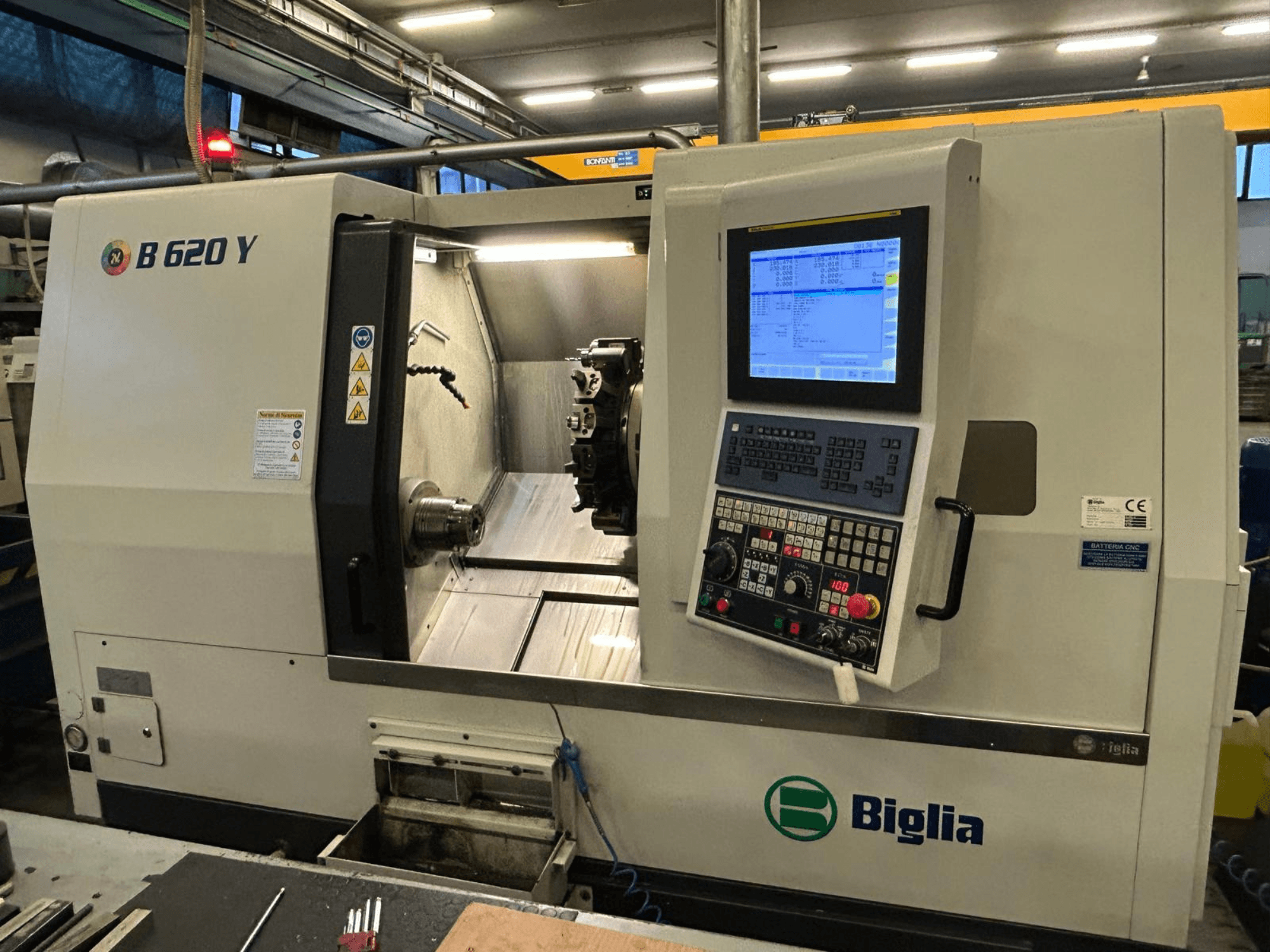Tokarka CNC Biglia B 620 Y w warsztacie, widok z przodu, pokazujący panel sterowania z wyświetlaczem cyfrowym i komponenty do obróbki.