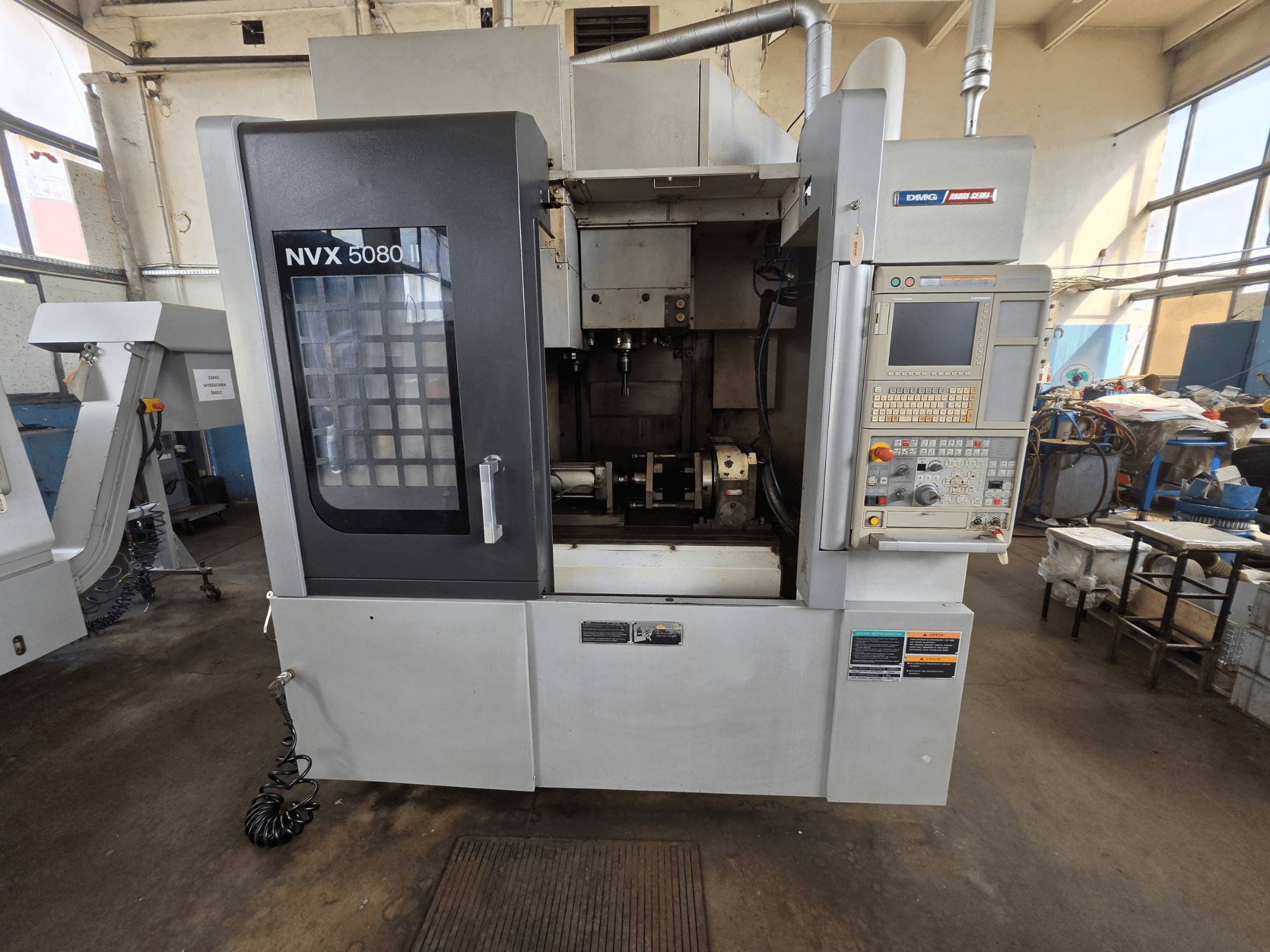 Widok z przodu pionowego centrum obróbczego DMG Mori Seiki NVX 5080 II/40 z panelem sterowania i przezroczystym okienkiem, ukazującym obszar obróbki.