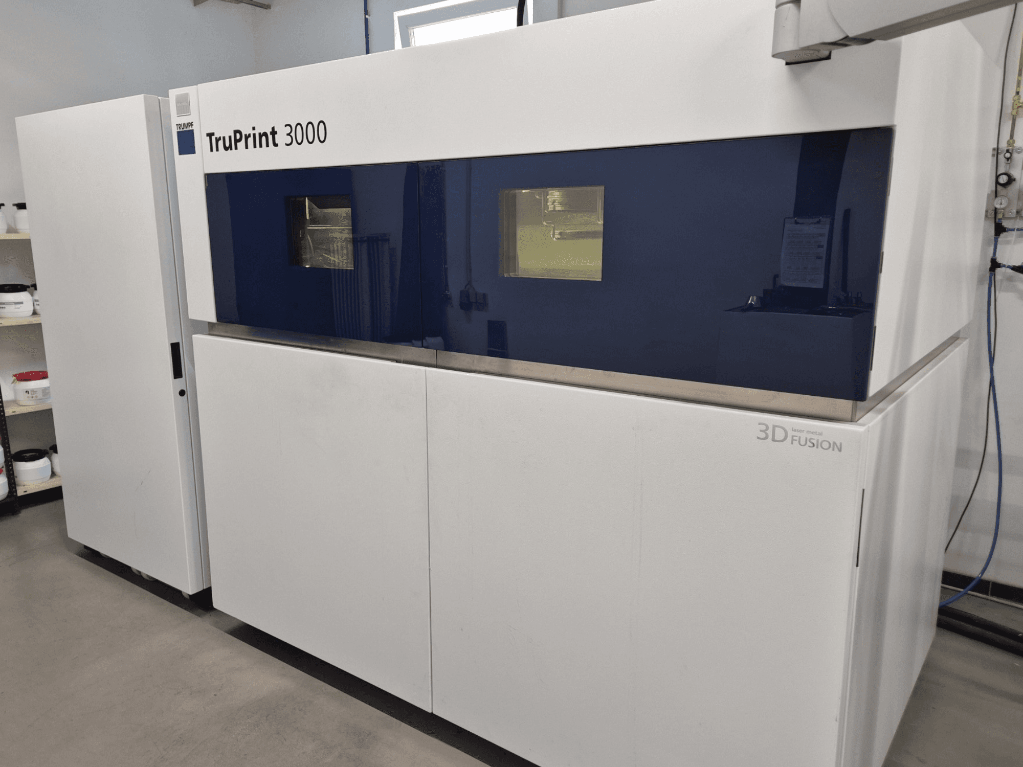 Drukarka 3D do metalu TruPrint 3000 w widoku z przodu, z niebieskim panelem i technologią stapiania laserowego.