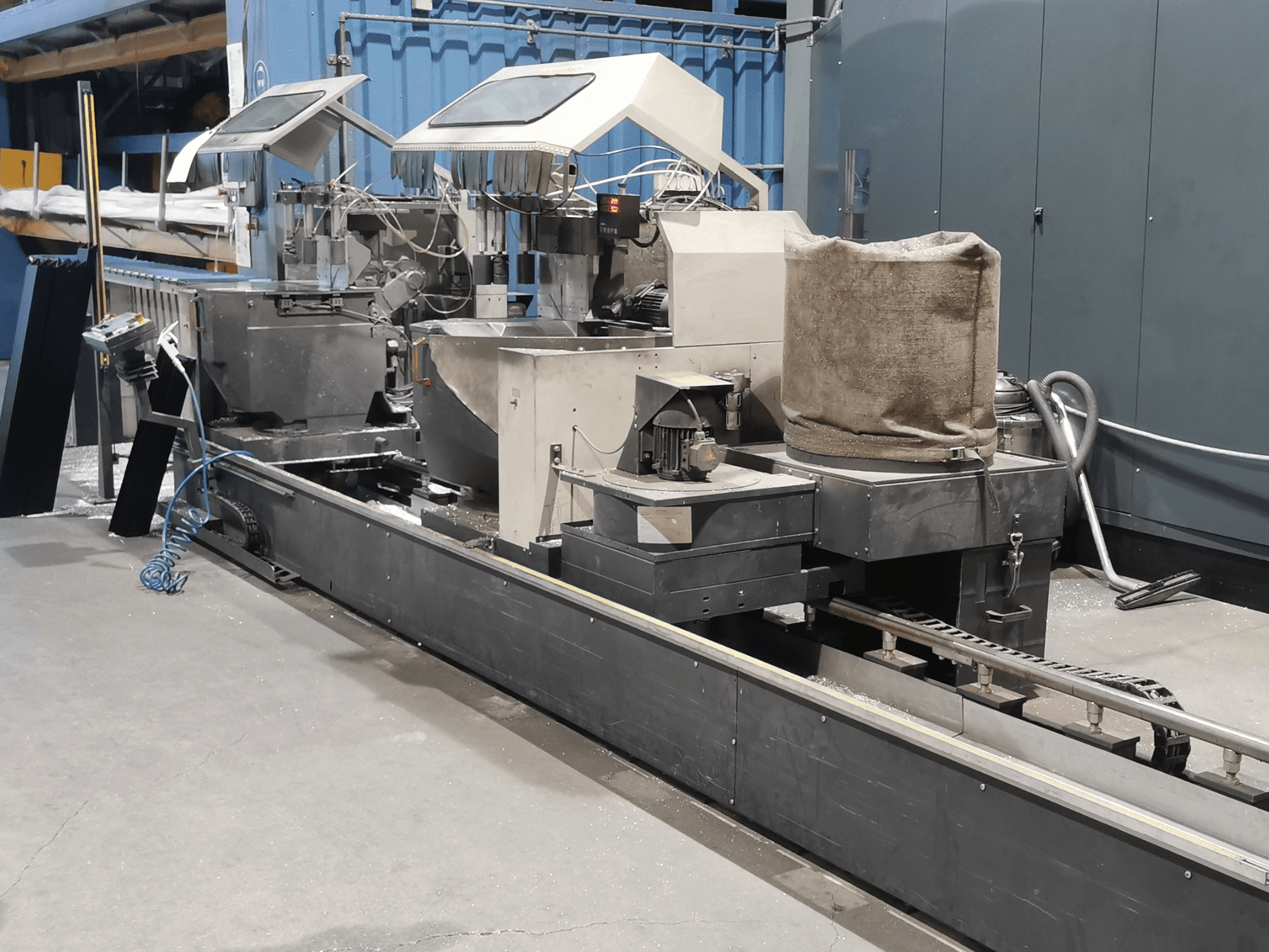 Przemysłowa maszyna przetwórcza widziana z boku, z lejami zasypowymi, przenośnikiem taśmowym i panelem sterowania, w warunkach fabrycznych.