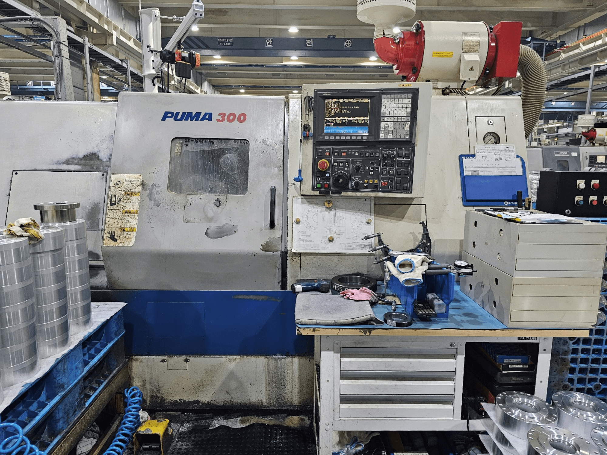 Maszyna CNC PUMA 300 w warsztacie; widok z przodu przedstawiający panel sterowania, narzędzia i metalowe części na stole warsztatowym.