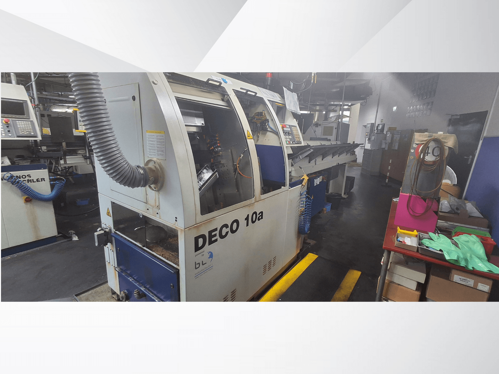 Maszyna CNC DECO 10a w warsztacie, widok z przodu; wyposażona w panel sterowania i system odsysania pyłu, w pobliżu stół warsztatowy.
