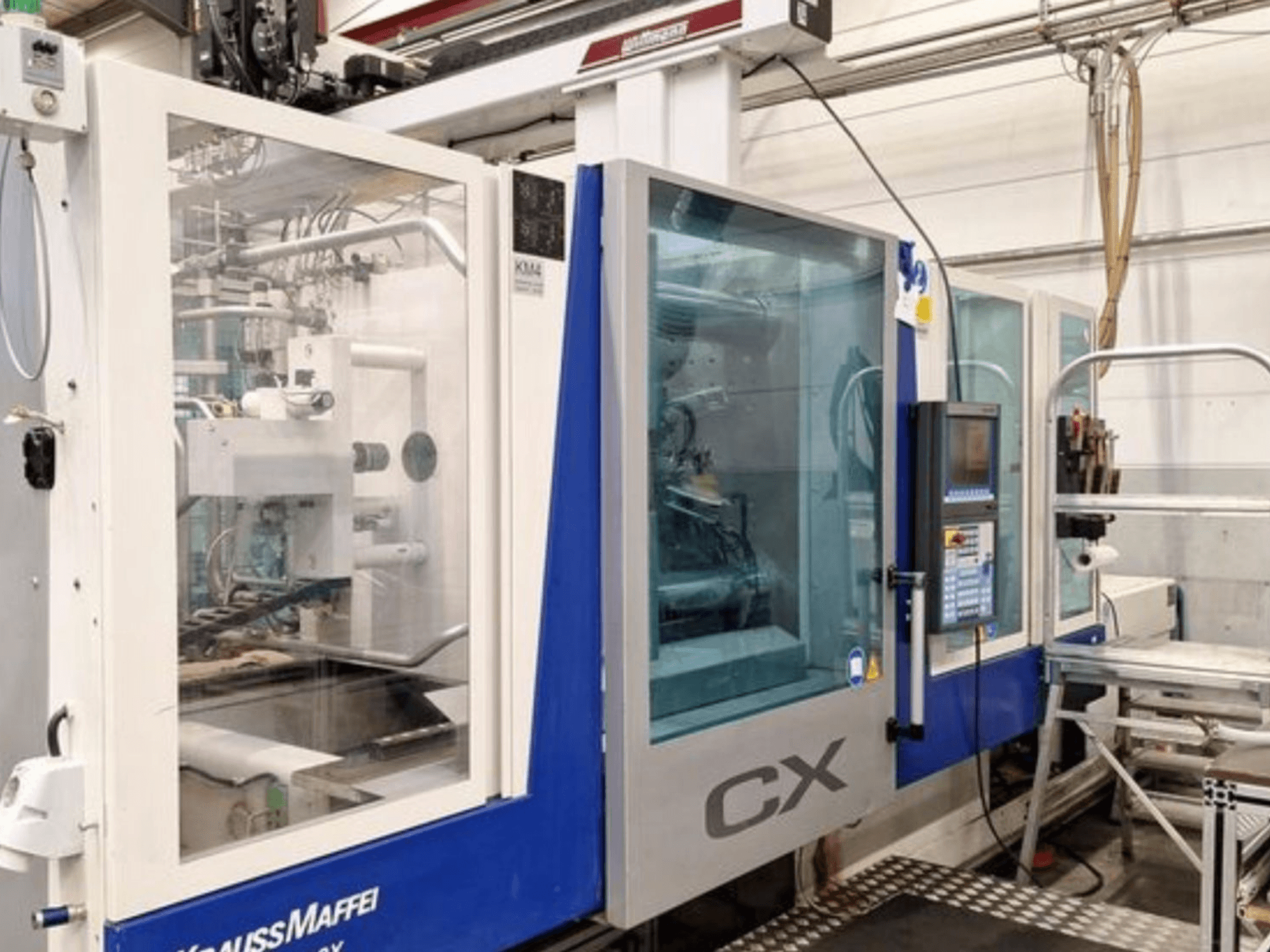 Hydrauliczna wtryskarka Krauss Maffei 300-1400 CX, widok z boku, przedstawiająca panel sterowania i przezroczystą obudowę.