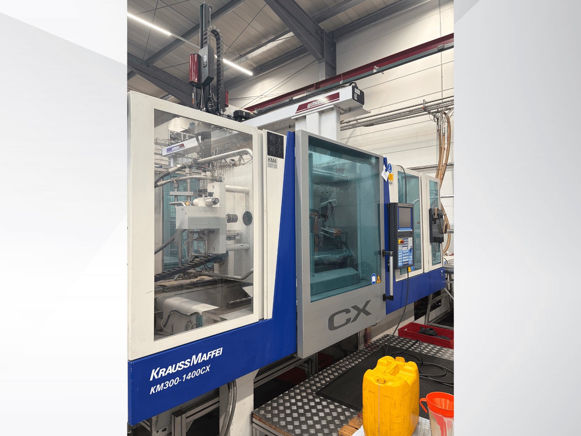 Hydrauliczna wtryskarka Krauss Maffei 300-1400 CX, widok z przodu z panelem sterowania i przezroczystą osłoną ochronną.