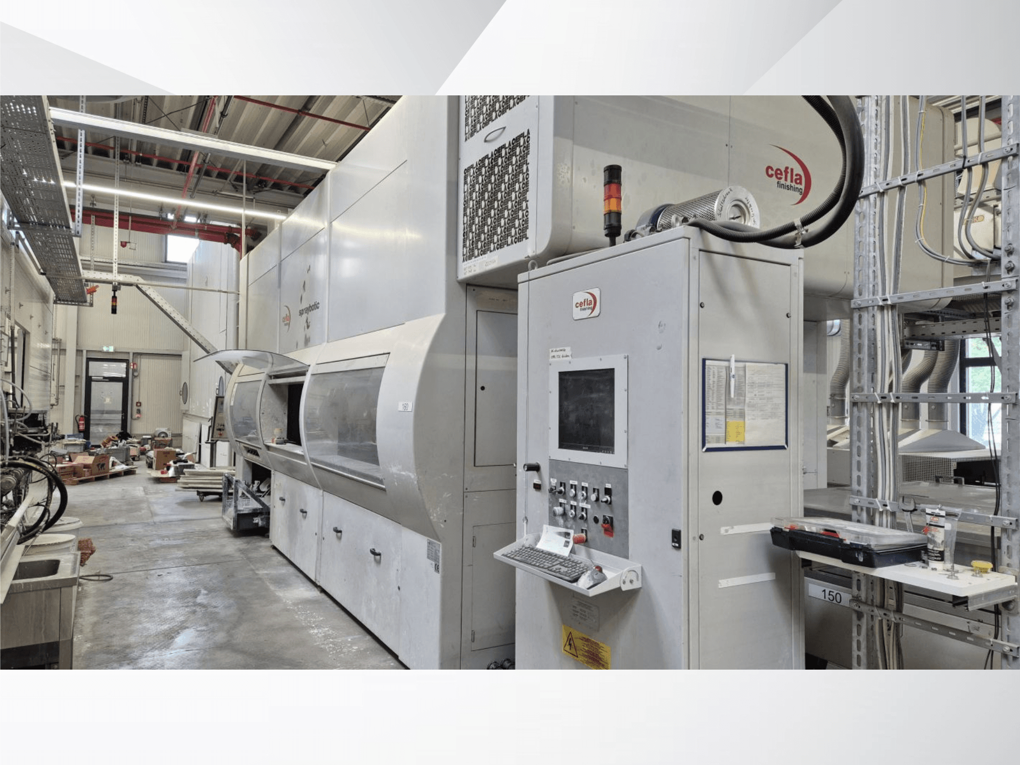 Linia produkcyjna Cefla Spraybotic MD w hali produkcyjnej – widok z przodu przedstawiający panel sterowania oraz komorę natryskową z przezroczystą pokrywą.