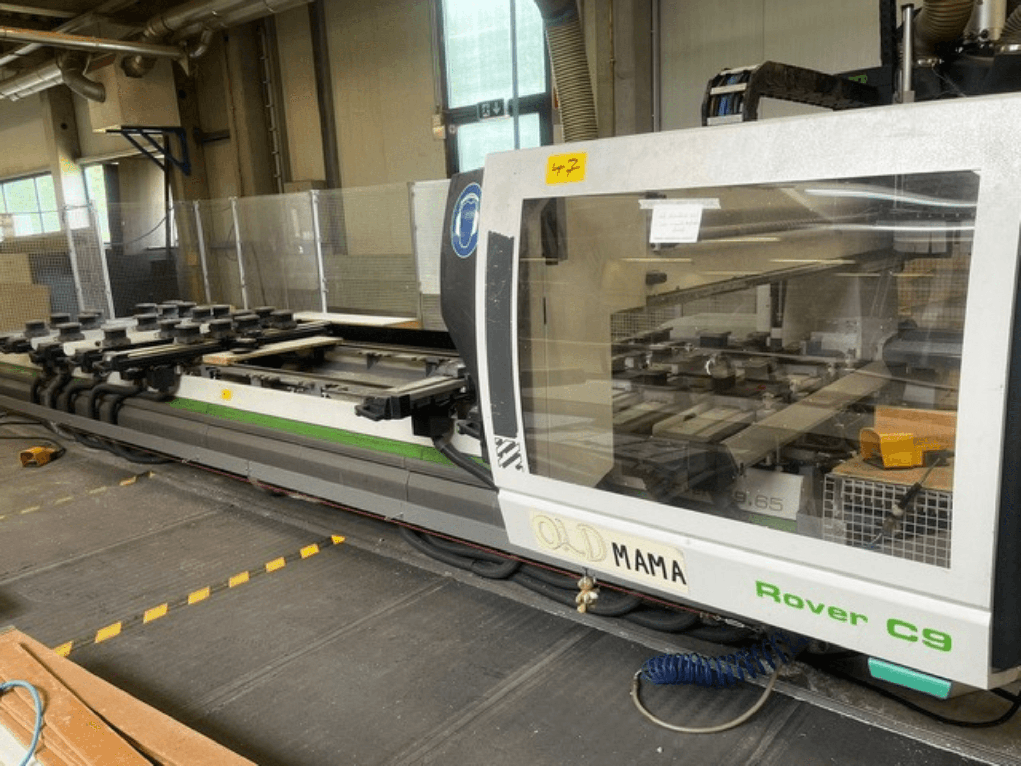 Frezarka CNC BIESSE Rover C 9.65 w warsztacie, widok z boku przedstawiający panel sterowania i stół roboczy z zaciskami.