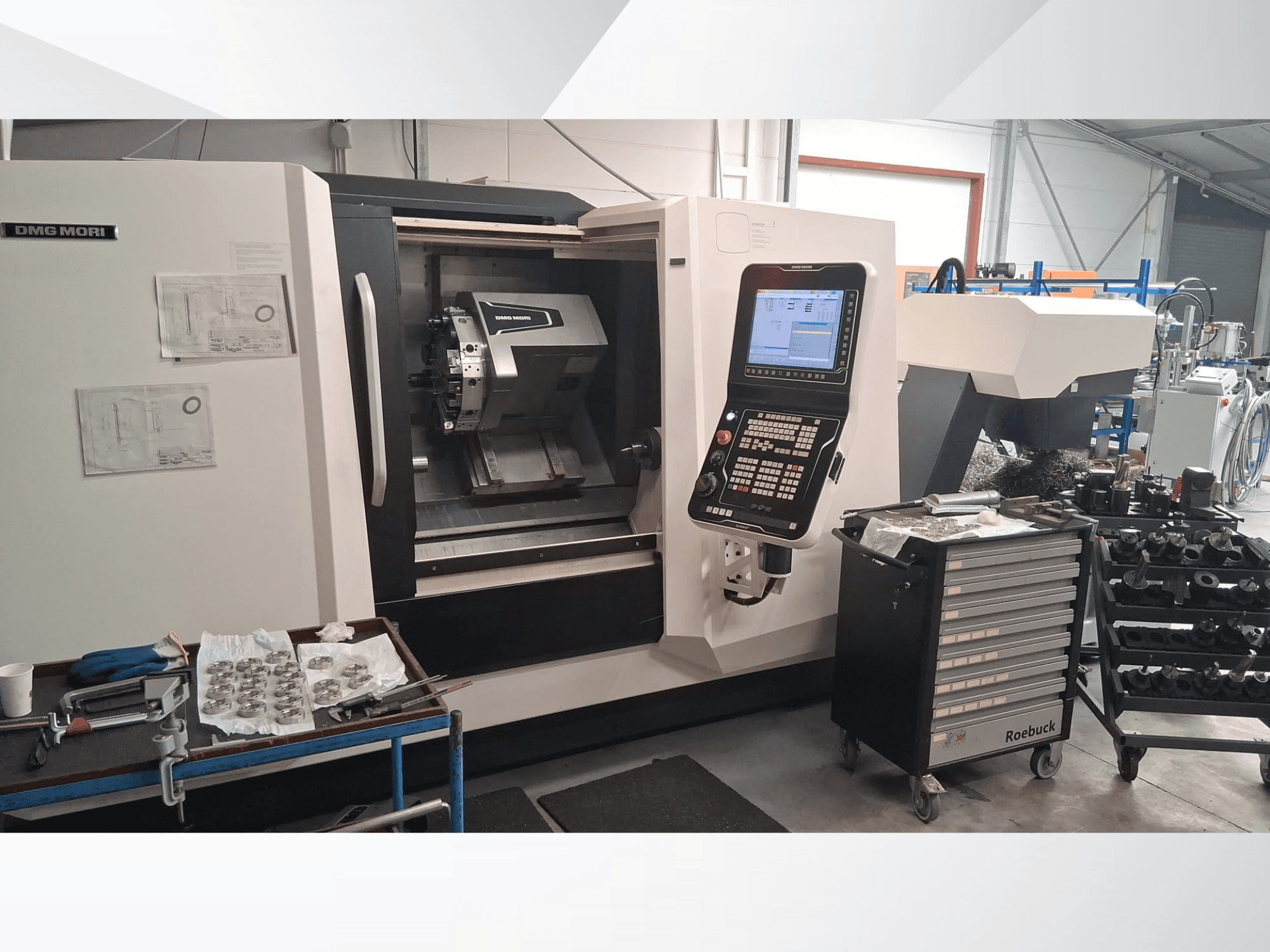Tokarka pozioma DMG MORI CLX450 w widoku z przodu, z panelem sterowania, obszarem roboczym, narzędziami i metalowymi częściami.
