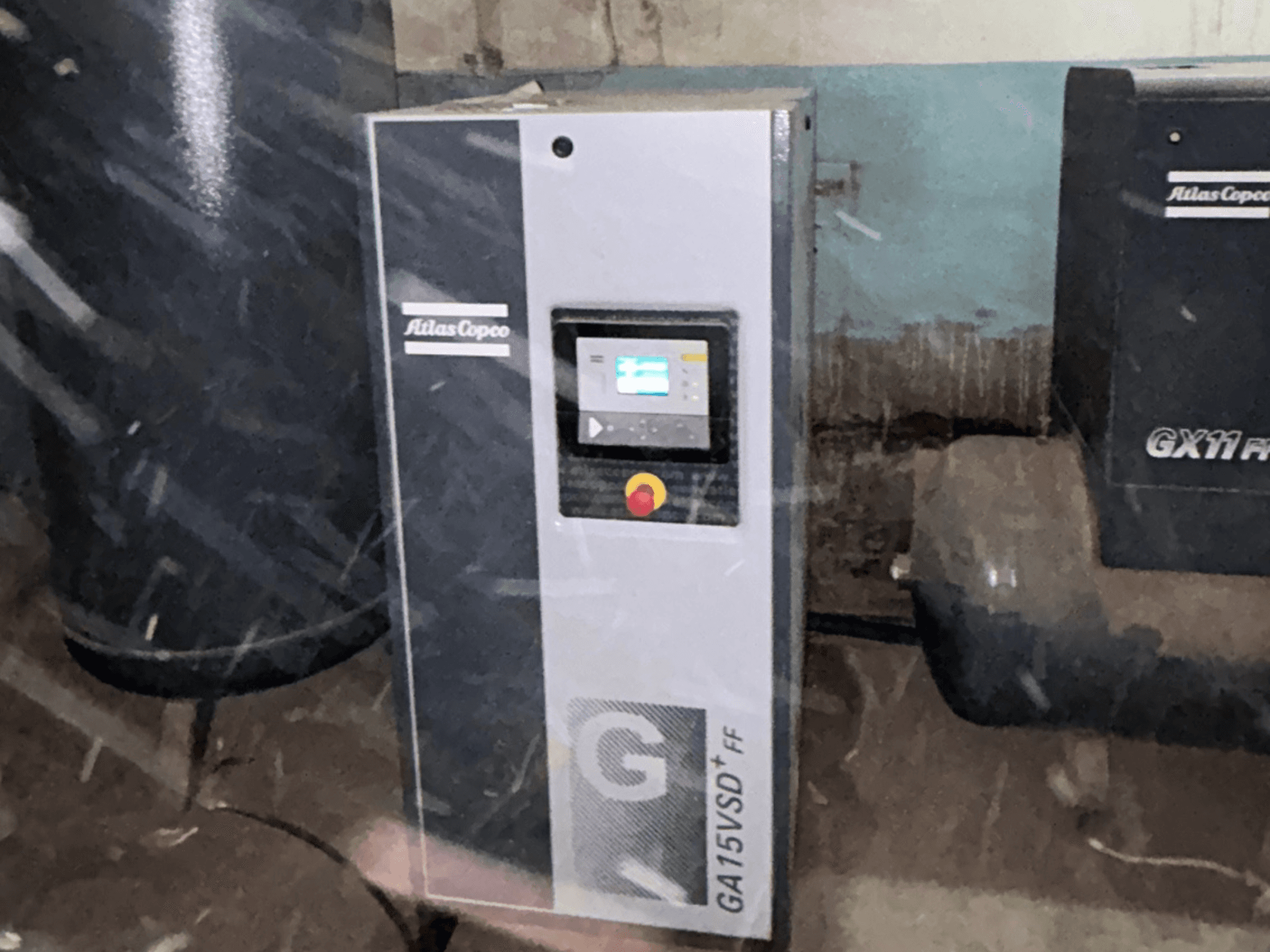Sprężarka powietrza Atlas Copco GA15VSD+FF, widok z przodu, wyposażona w panel sterowania z wyświetlaczem i czerwonym przyciskiem zatrzymania awaryjnego.