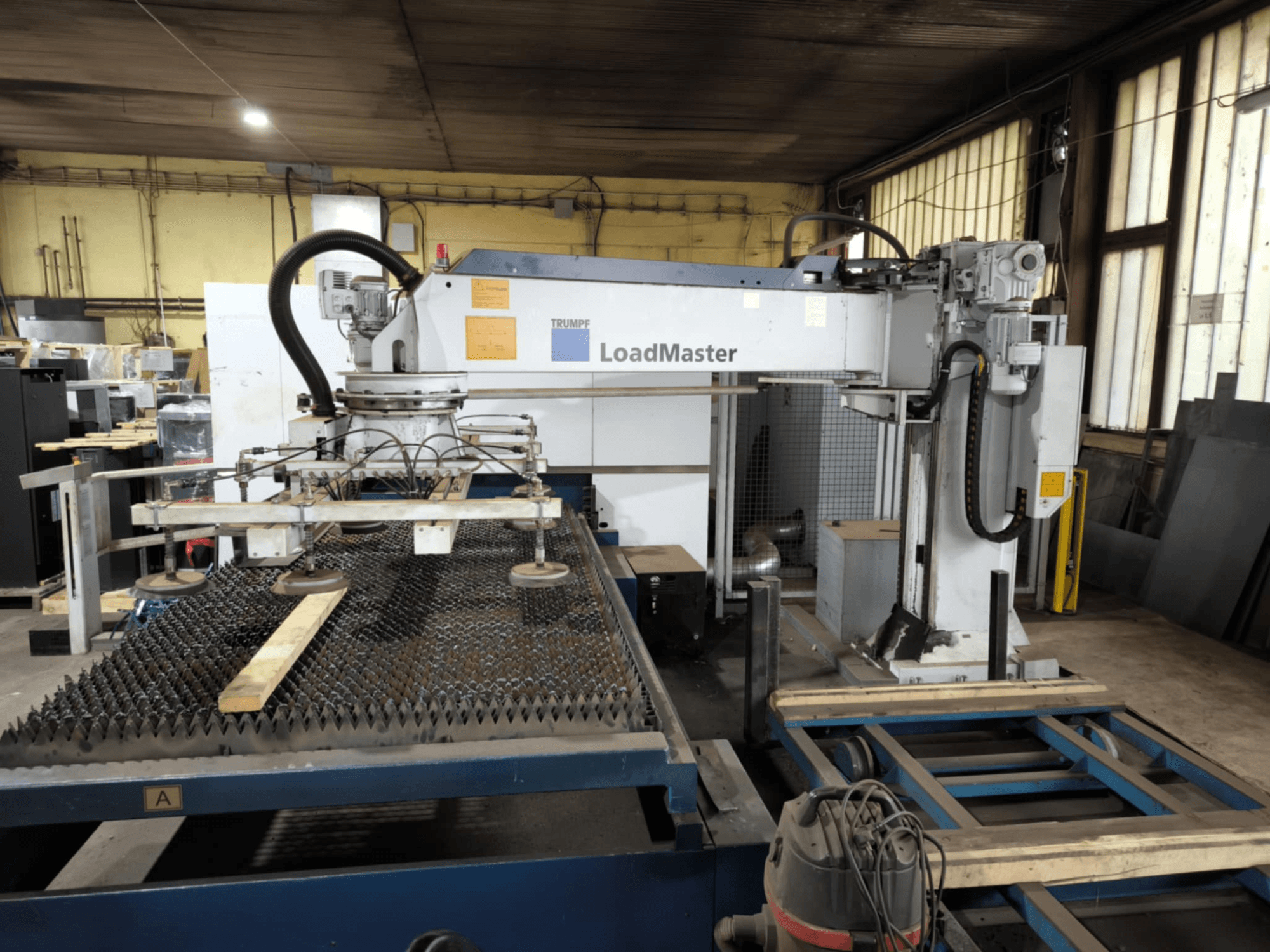 Maszyna do cięcia TRUMPF TRULASER 3030 FIBER, widok z przodu, prezentująca system LoadMaster i umieszczona na stole roboczym z rusztem.