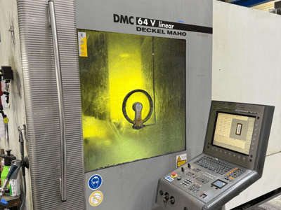 DMC 64 V linear firmy Deckel Maho, widok maszyny z przodu z panelem sterowania i żółtym przyciemnianym okienkiem pokazującym wewnętrzne mechanizmy.