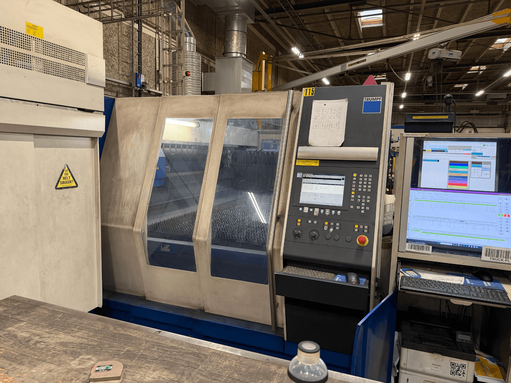 Widok z przodu przemysłowej maszyny laserowej Trumpf z panelem sterowania i wyświetlaczami cyfrowymi, ustawionej w środowisku fabrycznym.