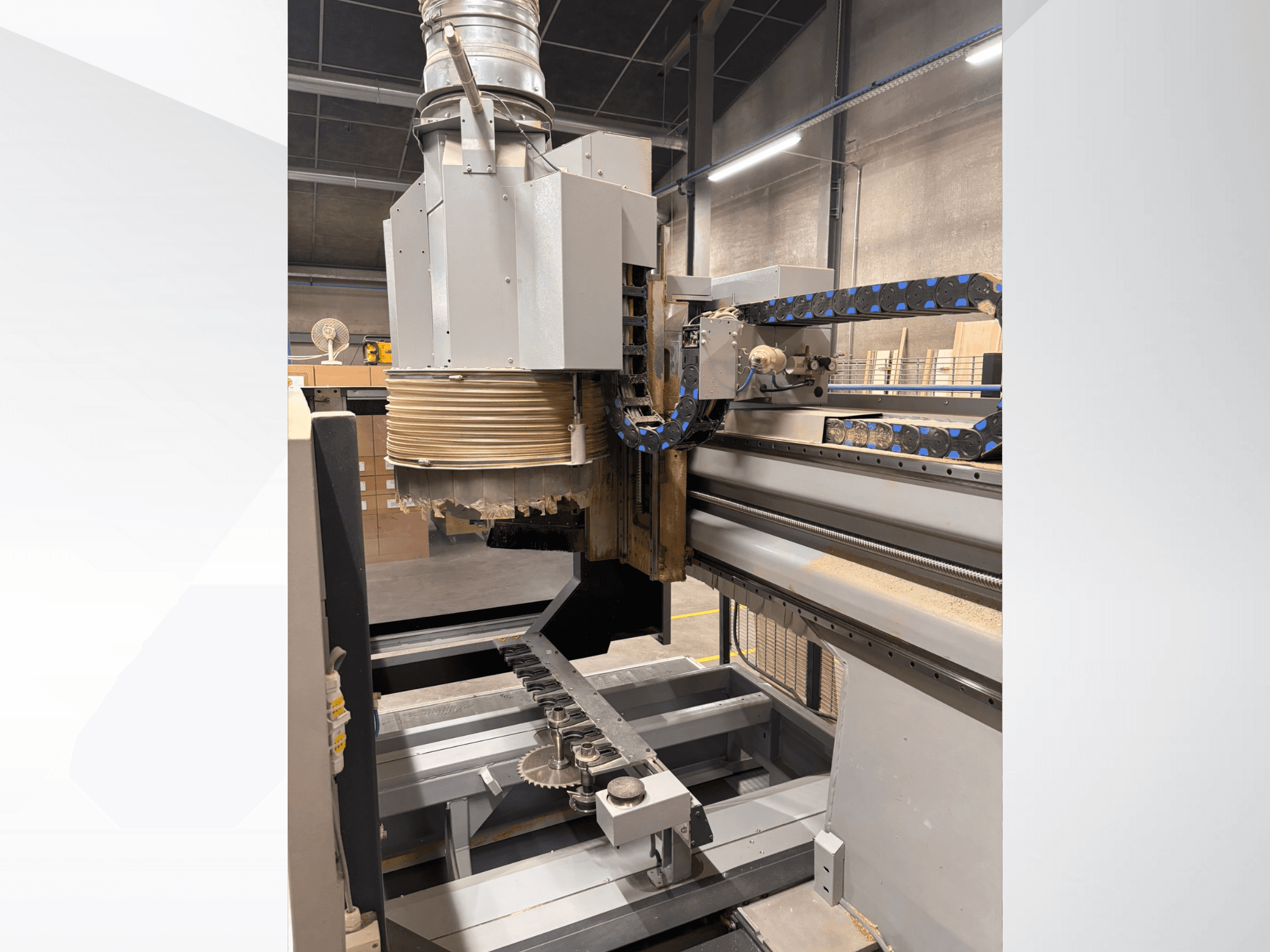 Frezarka CNC z dużym wrzecionem i przenośnikiem, widok z boku, pokazująca narzędzia do cięcia drewna i komponenty maszyny.