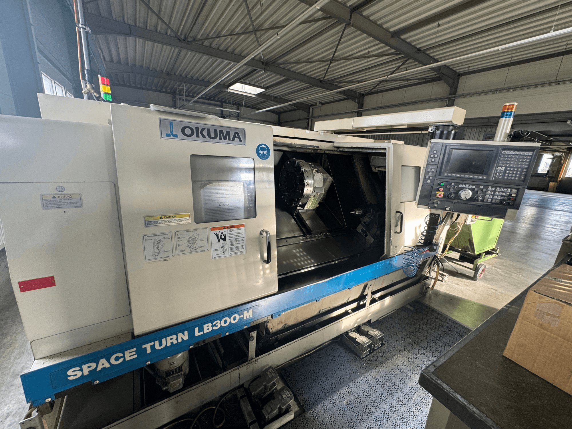 Tokarka CNC Okuma Space Turn LB300-M w widoku z przodu, z panelem sterowania i otwartymi drzwiami odsłaniającymi wewnętrzny obszar obróbki.