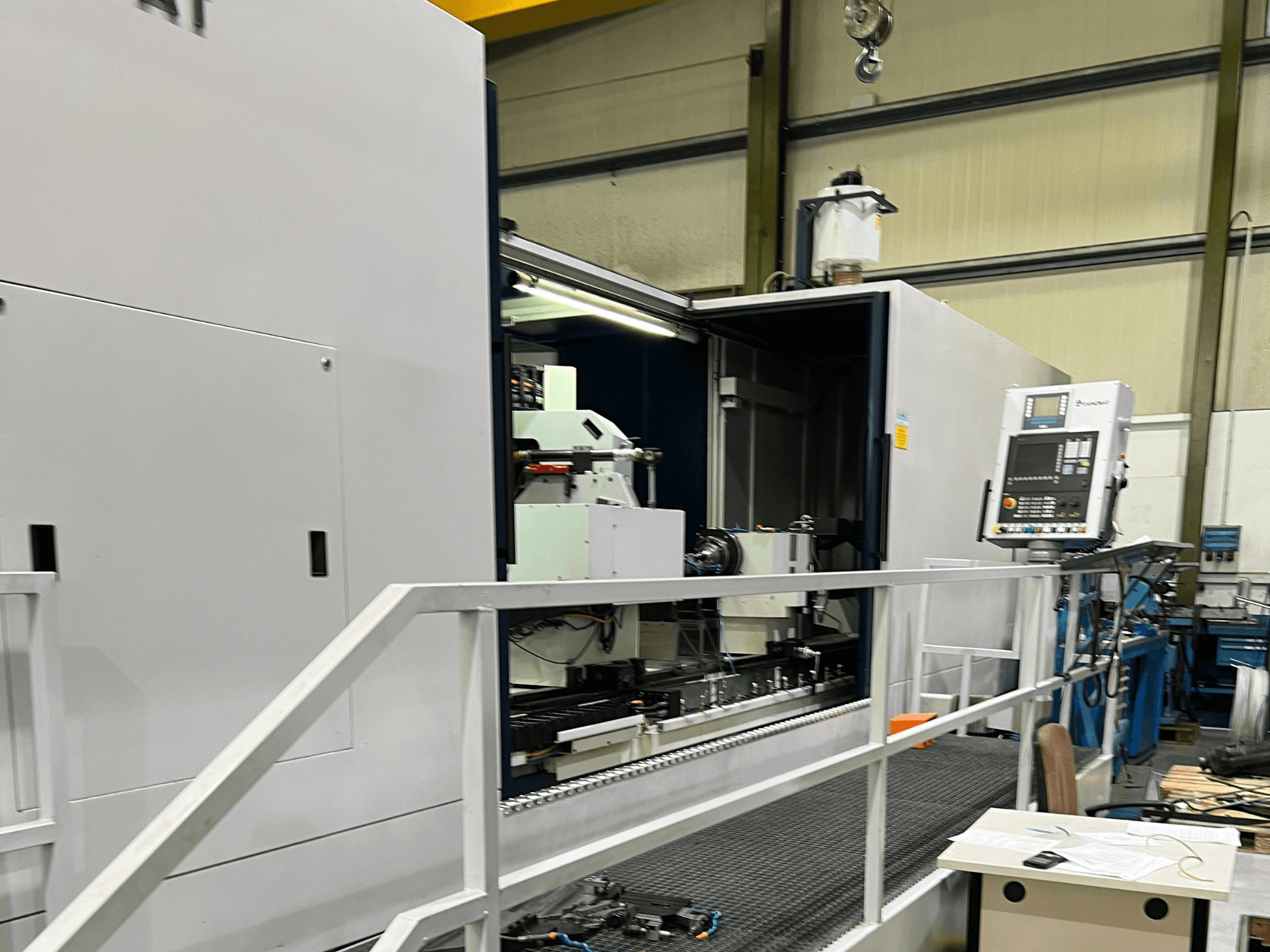 Centrum obróbcze CNC z otwartym widokiem z boku, pokazujące elementy sterujące, uchwyt narzędziowy i główny element wewnątrz. Szczegóły marki nie są widoczne.