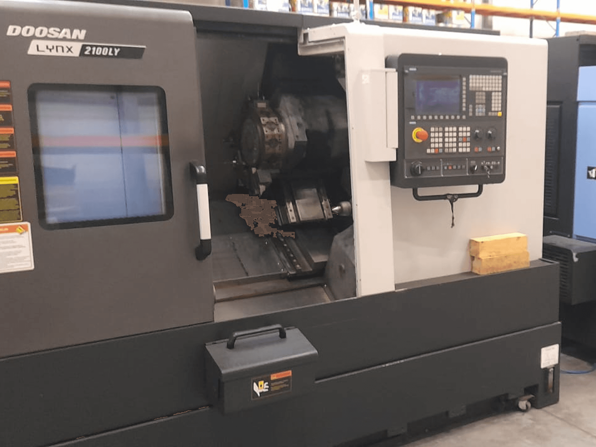Tokarka CNC Doosan Lynx 2100LY, widok z przodu przedstawiający panel sterowania, uchwyt narzędziowy i wewnętrzną przestrzeń roboczą; widoczne etykiety techniczne.