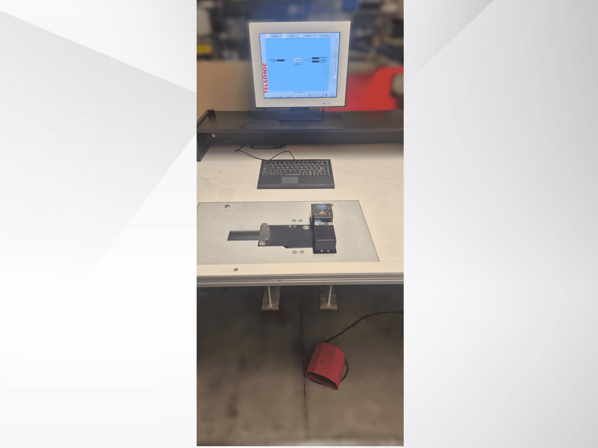 Widok z góry na stację testową z monitorem komputera, klawiaturą i panelem sterowania z przyciskiem i zielonym światłem.