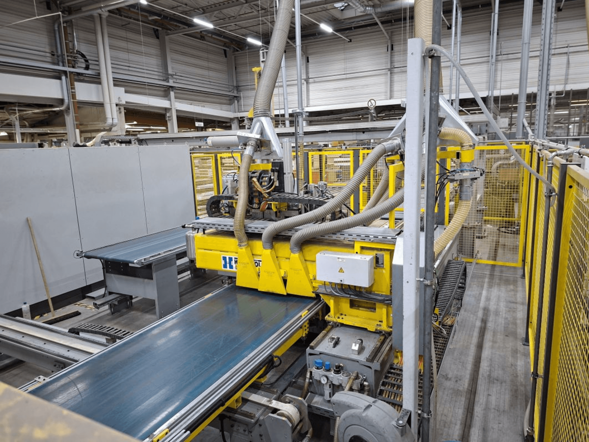 System przenośników przemysłowych w widoku z boku, z żółtymi maszynami, panelem sterowania i przyłączami węży do produkcji.