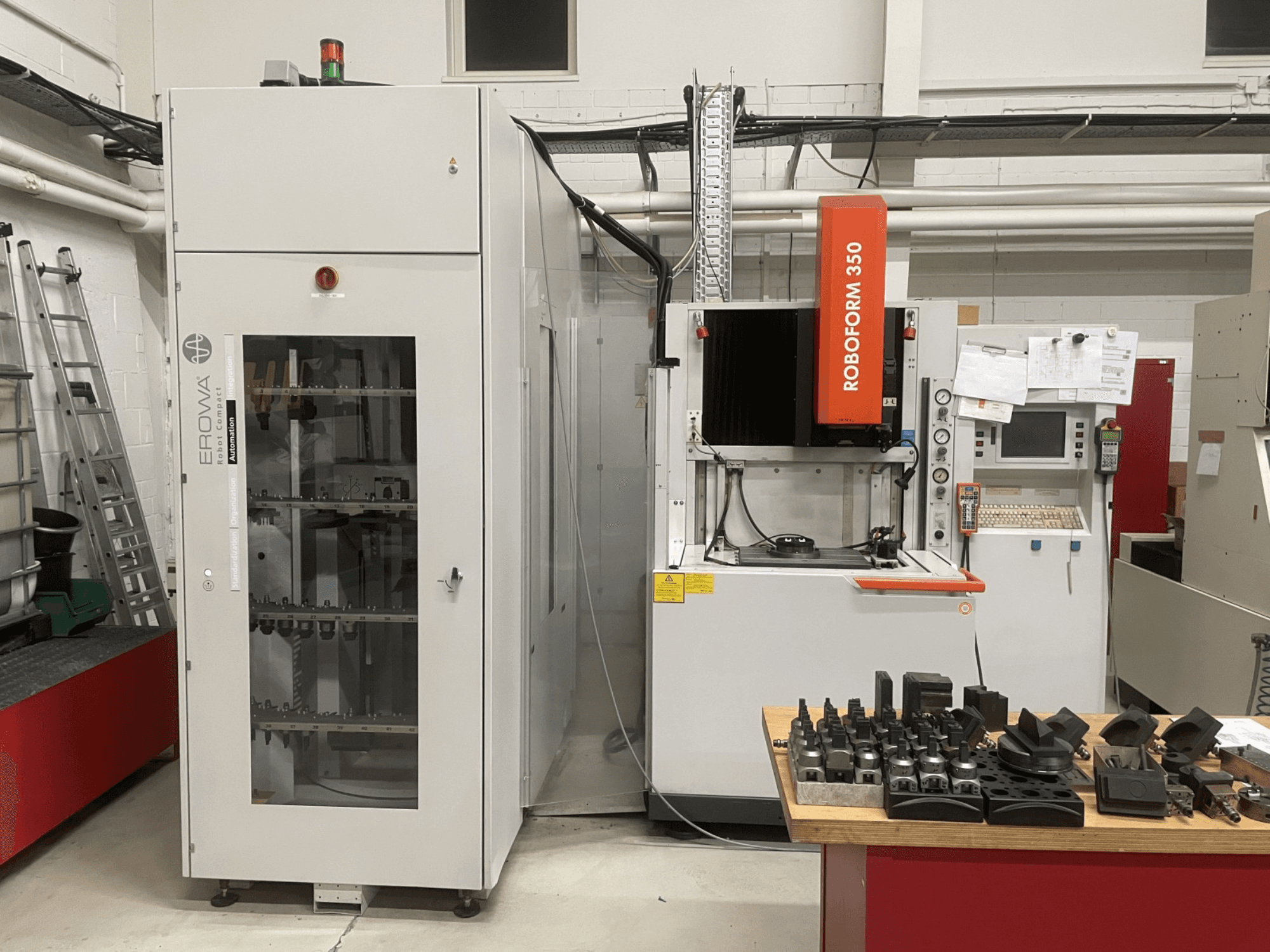 Elektrodrążarka wgłębna CHARMILLES Roboform 350, widok z przodu, z narzędziami wyświetlanymi na stole i sąsiednim wyposażeniem.