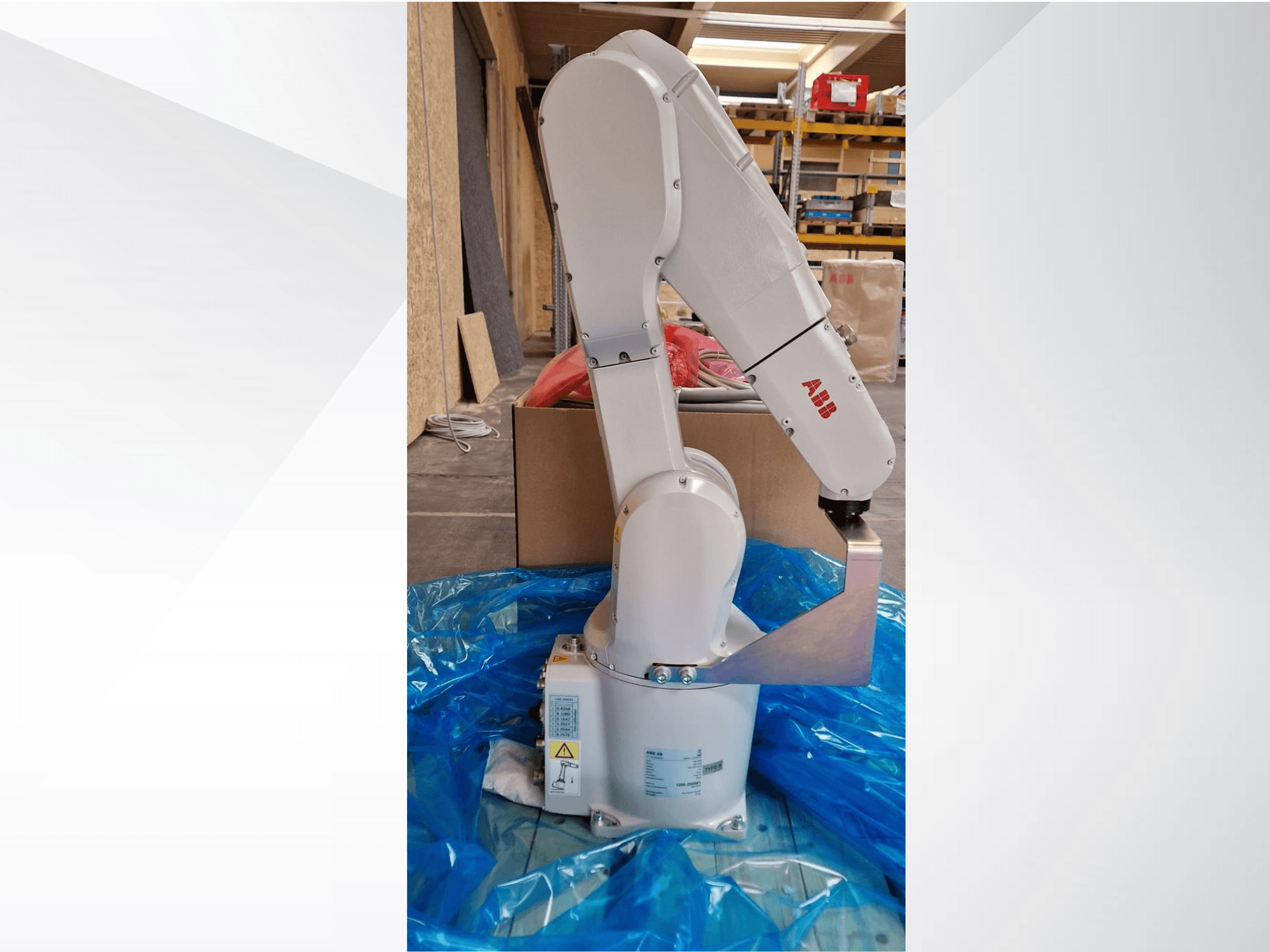 Model ramienia robota ABB, widok z boku na niebieskiej plandece, prezentujący przeguby i metalowy efektor końcowy, z widocznymi etykietami technicznymi.
