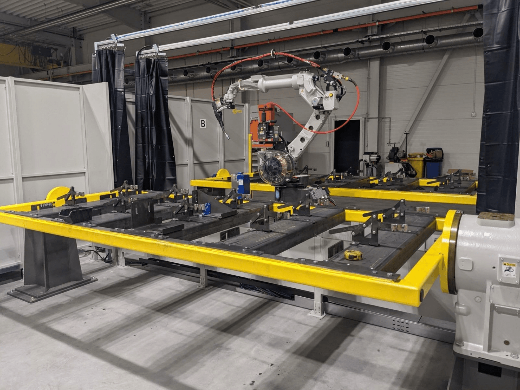 Widok z przodu ramienia robota PANASONIC TAWERS TM-2000WG3 umieszczonego nad żółtym stołem roboczym z metalowymi elementami przeznaczonymi do montażu.