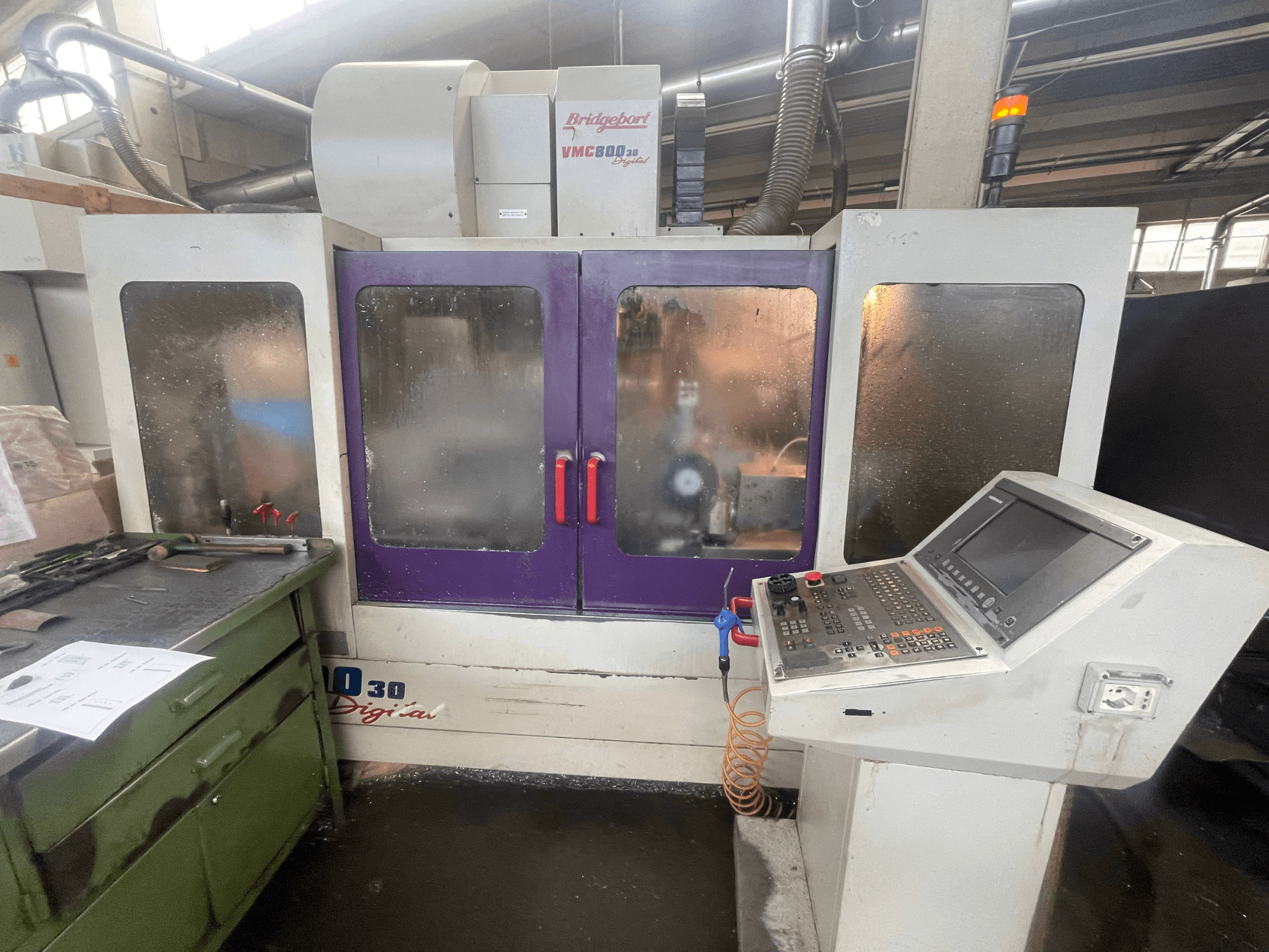 Pionowe centrum obróbcze Bridgeport VMC 800/30, widok z przodu, z widocznym panelem sterowania i fioletowymi drzwiczkami oraz narzędziami na sąsiedniej powierzchni.