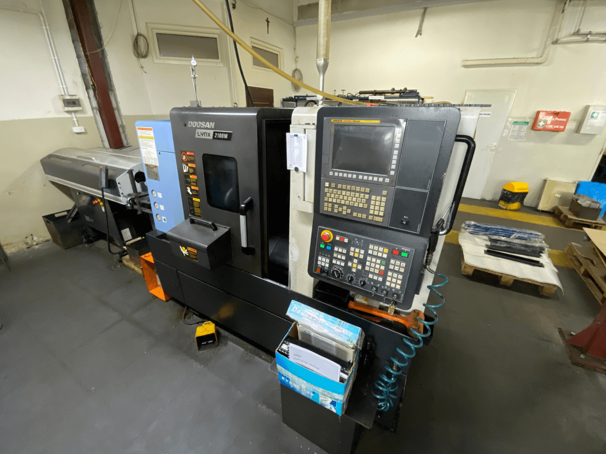 Tokarka pozioma DOOSAN LYNX 2100MA widziana z boku, z panelem sterowania, narzędziami i obszarem roboczym.