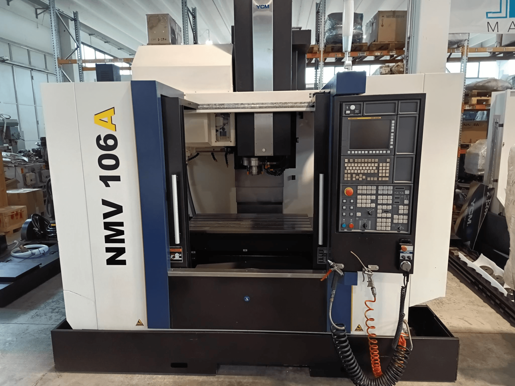 Centrum obróbcze YCM NMV 106A, widok z przodu, z panelem sterowania z przyciskami i wężami chłodziwa.