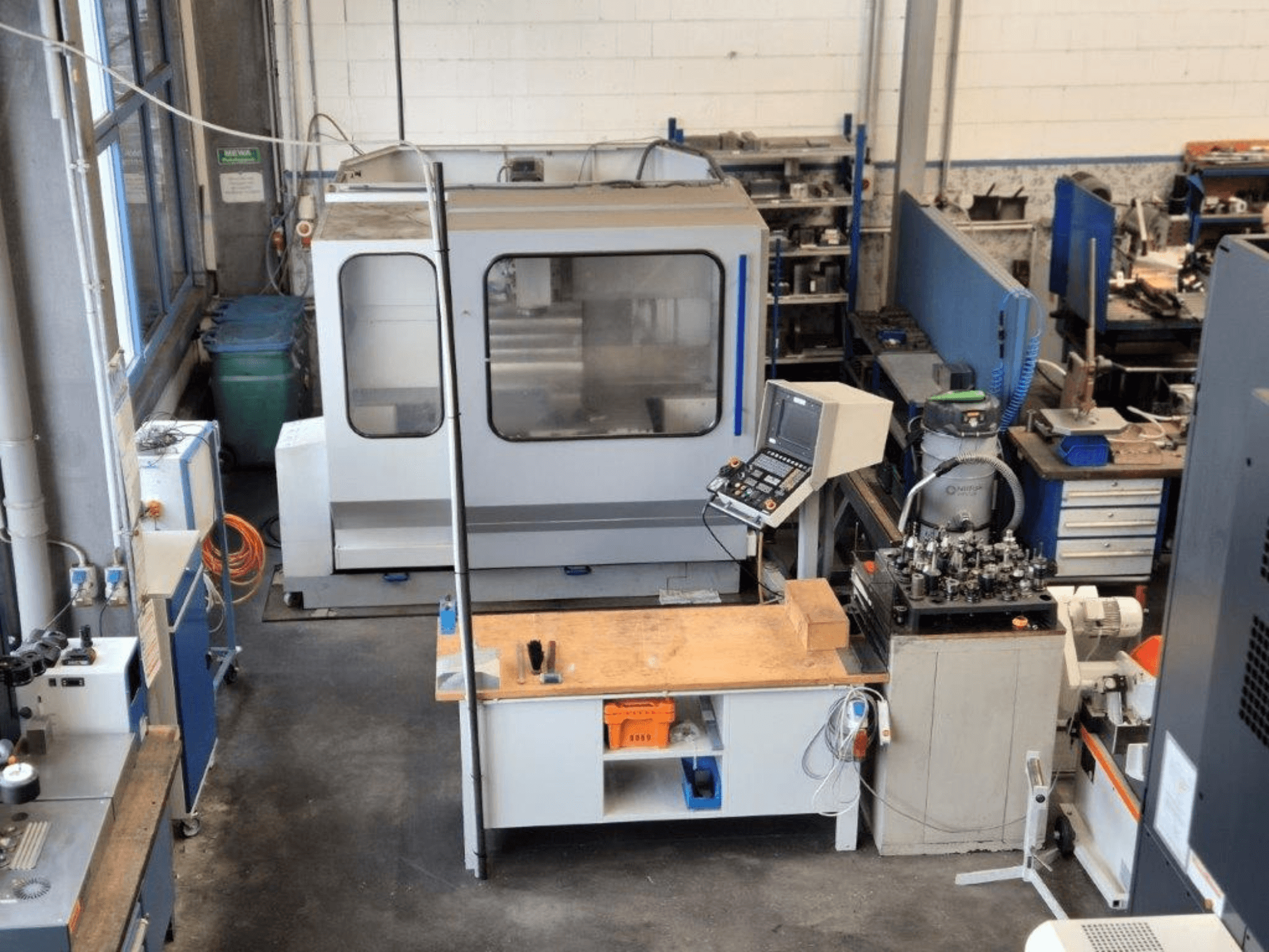 Frezarka CNC w warsztacie, widok z przodu, z panelem sterowania, powierzchnią roboczą i narzędziami widocznymi w tle.