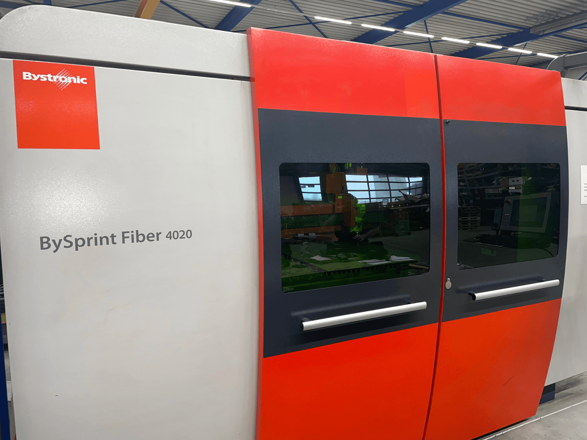 Bystronic BySprint Fiber 4020 w widoku z przodu, z szaro-czerwonym panelem z dużymi oknami i interfejsem sterowania widocznym wewnątrz.