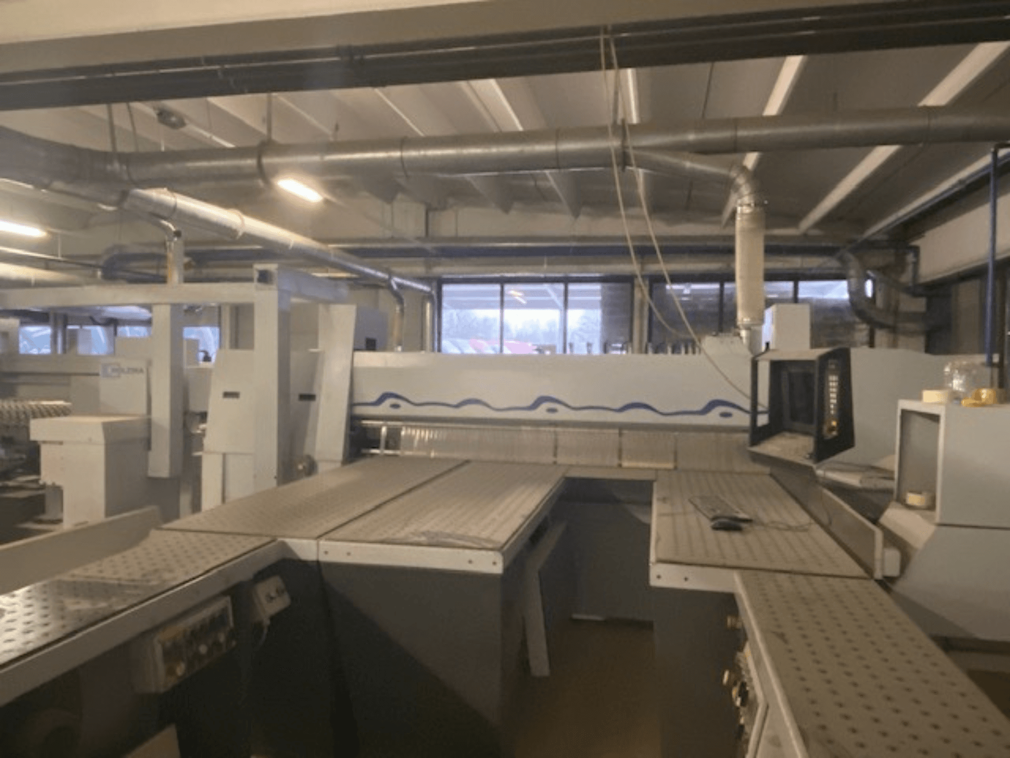 Przemysłowa przestrzeń robocza z zestawem maszyn i panelem sterowania, widziana z góry.