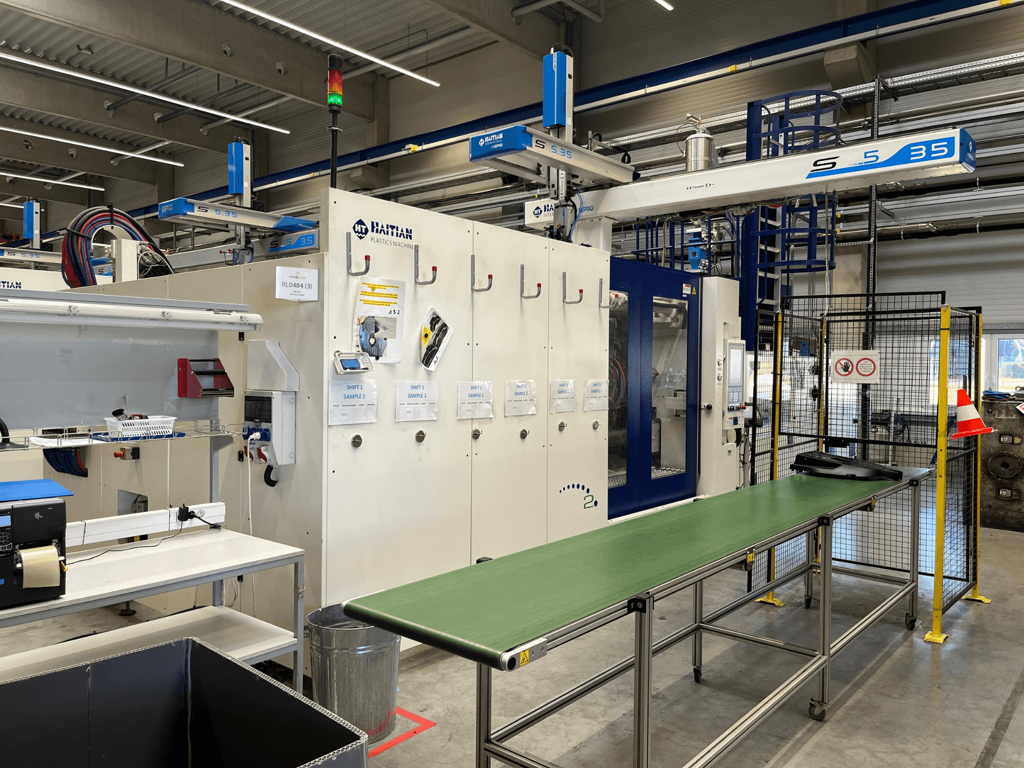 Haitańska maszyna do tworzyw sztucznych S5-35 w warsztacie; zielony stół przenośnika, bariery bezpieczeństwa i panel sterowania widoczne z przodu.