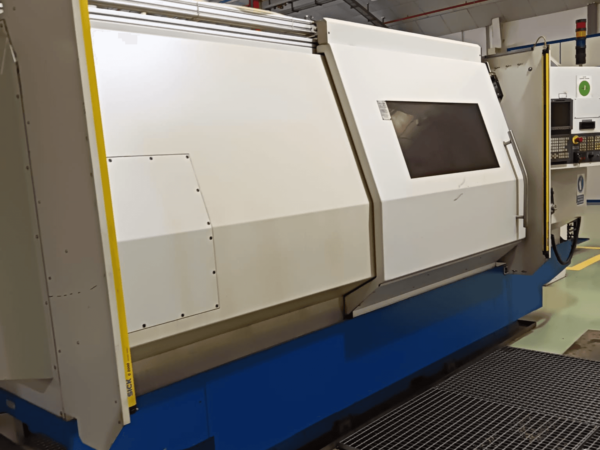 Tokarka przemysłowa, widok z boku, z dużą biało-niebieską obudową, cyfrowym panelem sterowania i funkcjami bezpieczeństwa.