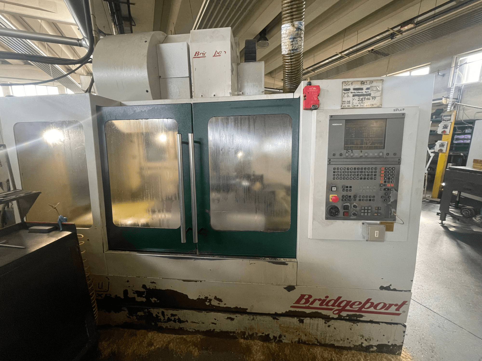 Pionowe centrum obróbcze Bridgeport VMC 1000/30, widok z przodu z panelem sterowania, na zdjęciu widać zużytą obudowę i zielone drzwiczki.