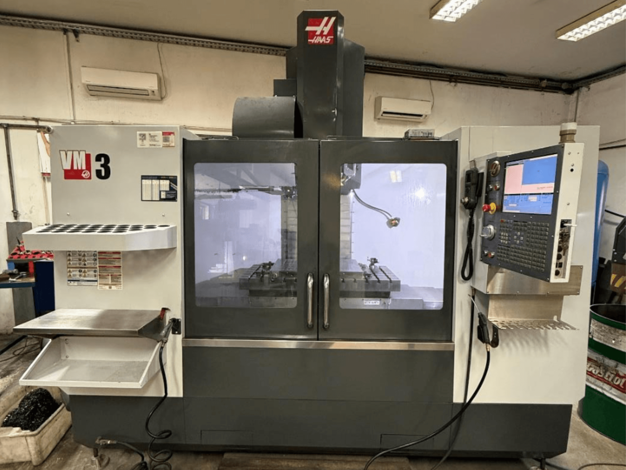 Pionowe centrum obróbcze Haas VM-3 widziane z przodu, wyposażone w duży panel sterowania oraz widoczną strefę roboczą z narzędziami.